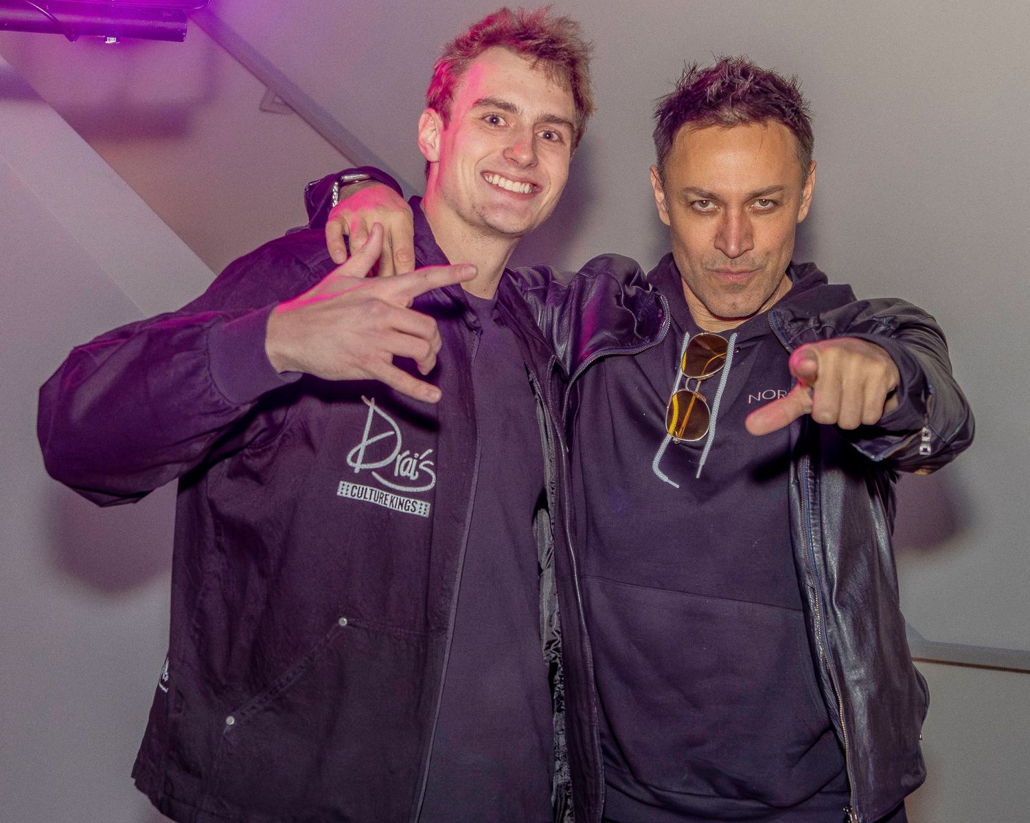 Two people posing together under purple lighting at indoor event.
