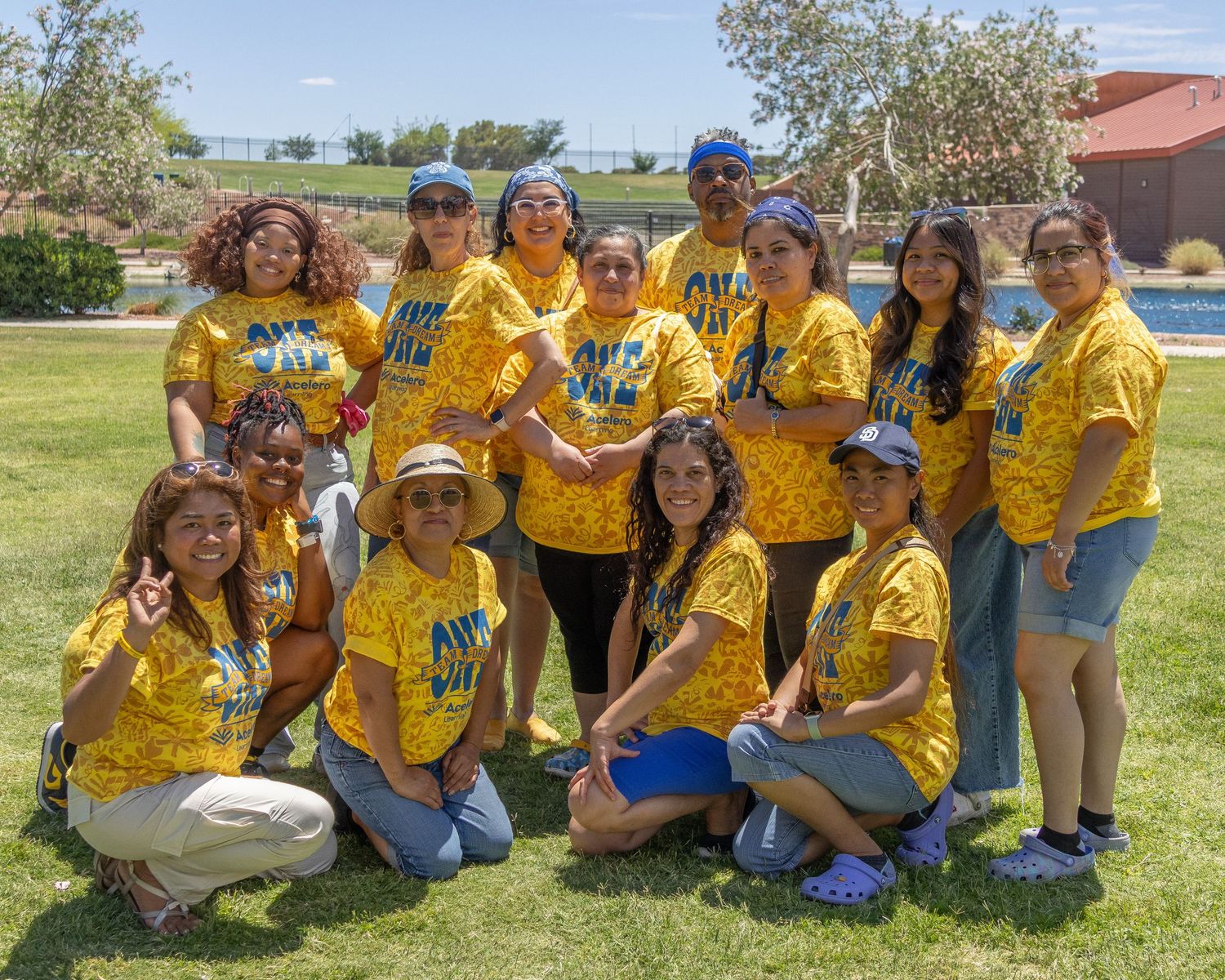 Group photo of team members in yellow shirts gathered on sunny grass field.
