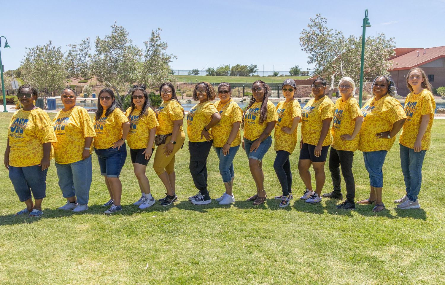 Large group in matching yellow shirts posed together on grass for panoramic photo.