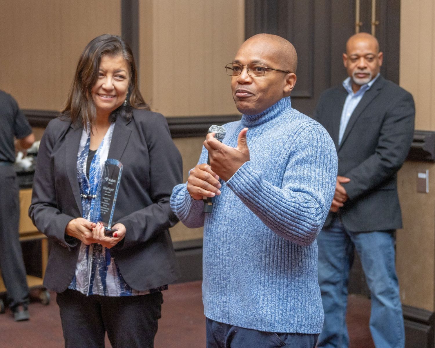 Speakers engage in presentation wearing business casual attire at indoor event.