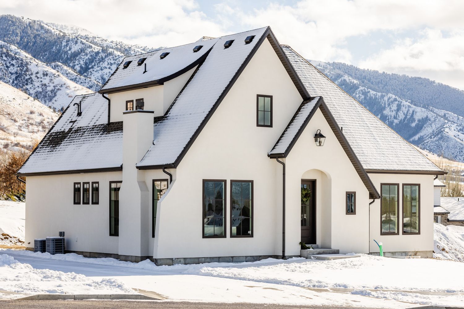 Modern white farmhouse exterior with snow-covered mountains in the background.