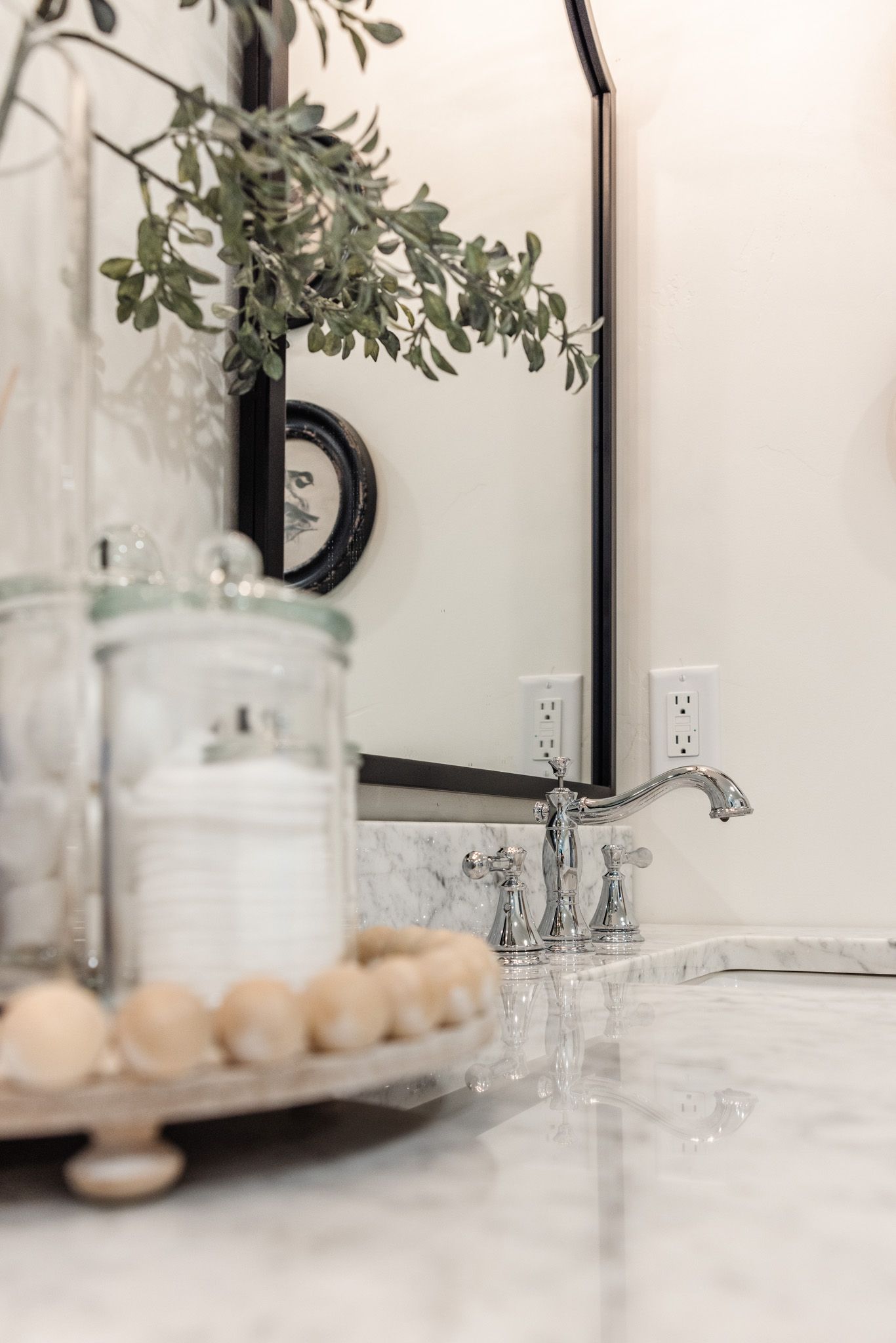 Elegant bathroom vanity with marble countertop and decorative greenery in glass vase.