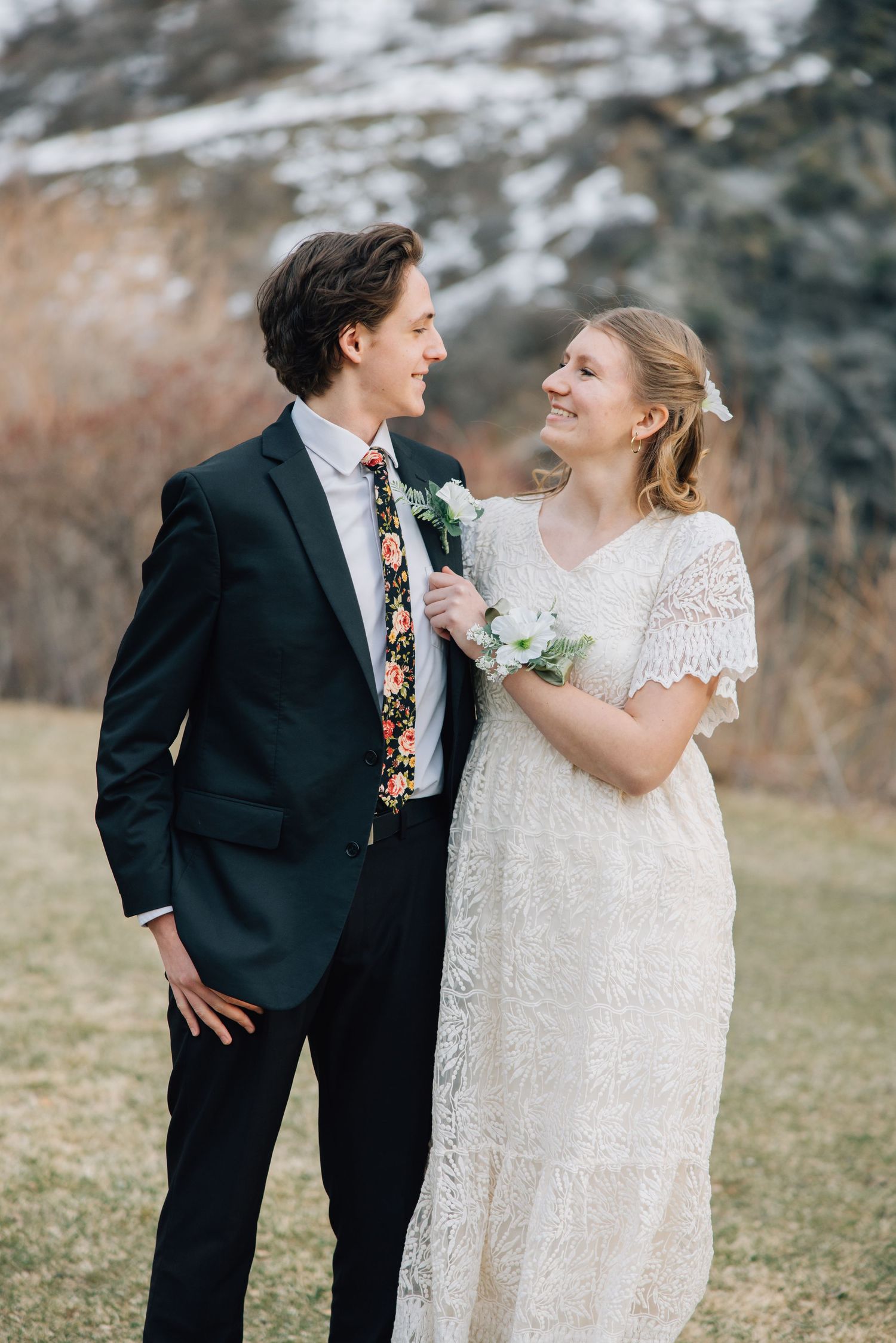 A couple in wedding attire share a playful moment outdoors in winter, with the bride in lace and groom in black suit.