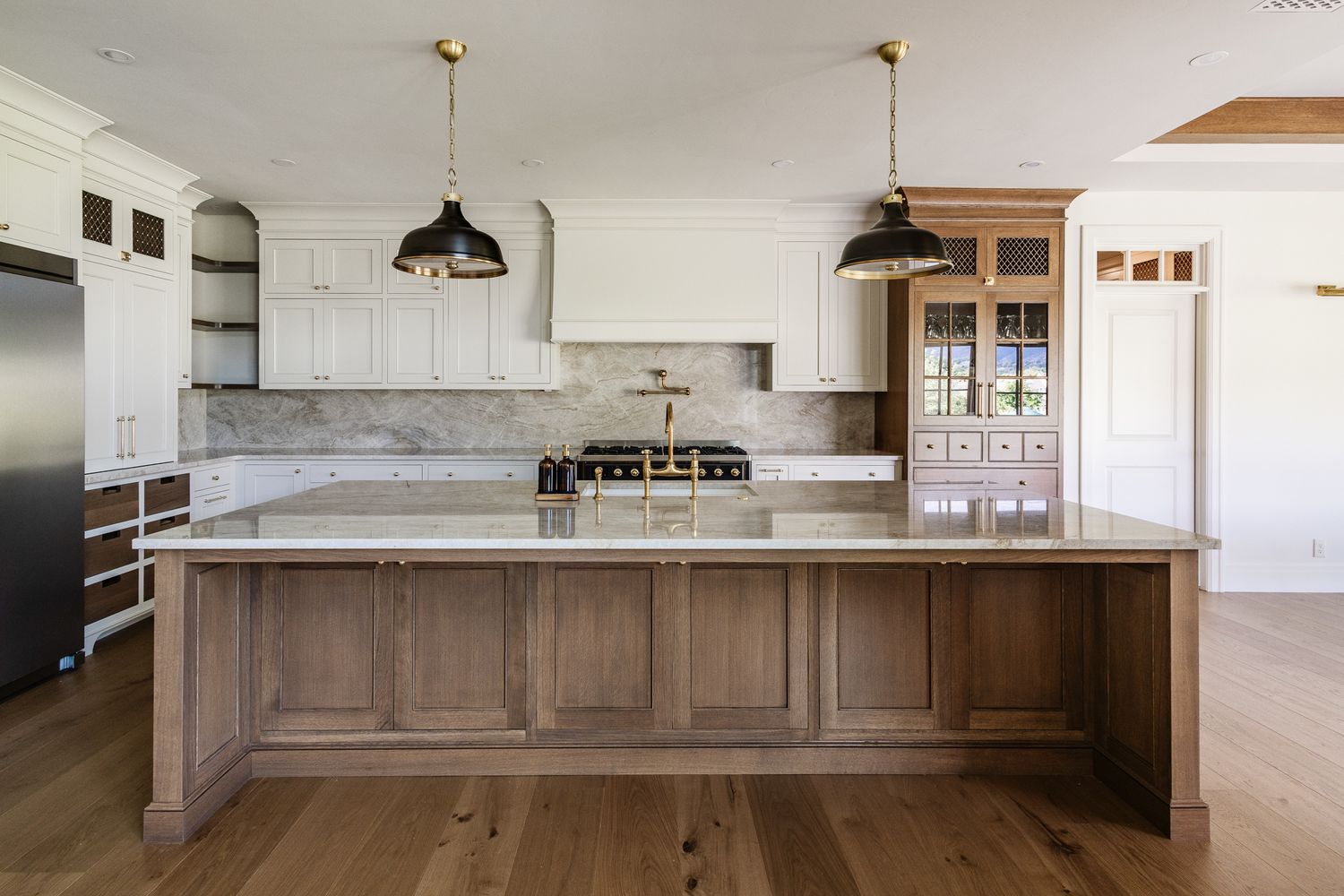 Modern white kitchen with marble countertops, wood cabinetry, and pendant lighting.
