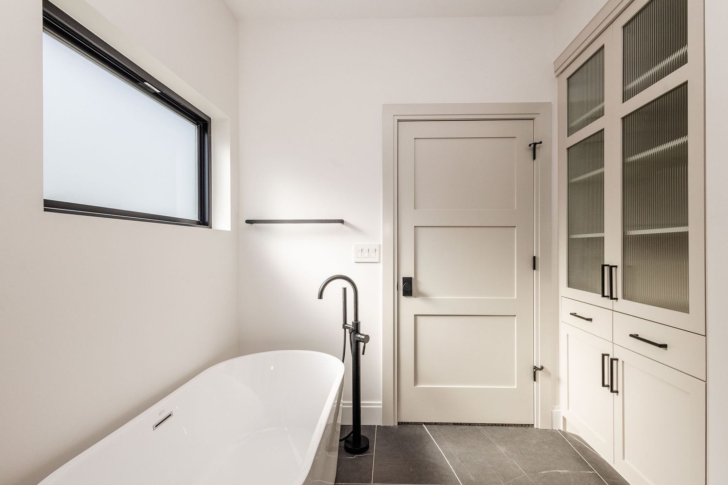 Modern bathroom featuring freestanding tub, glass cabinets, and matte black fixtures.