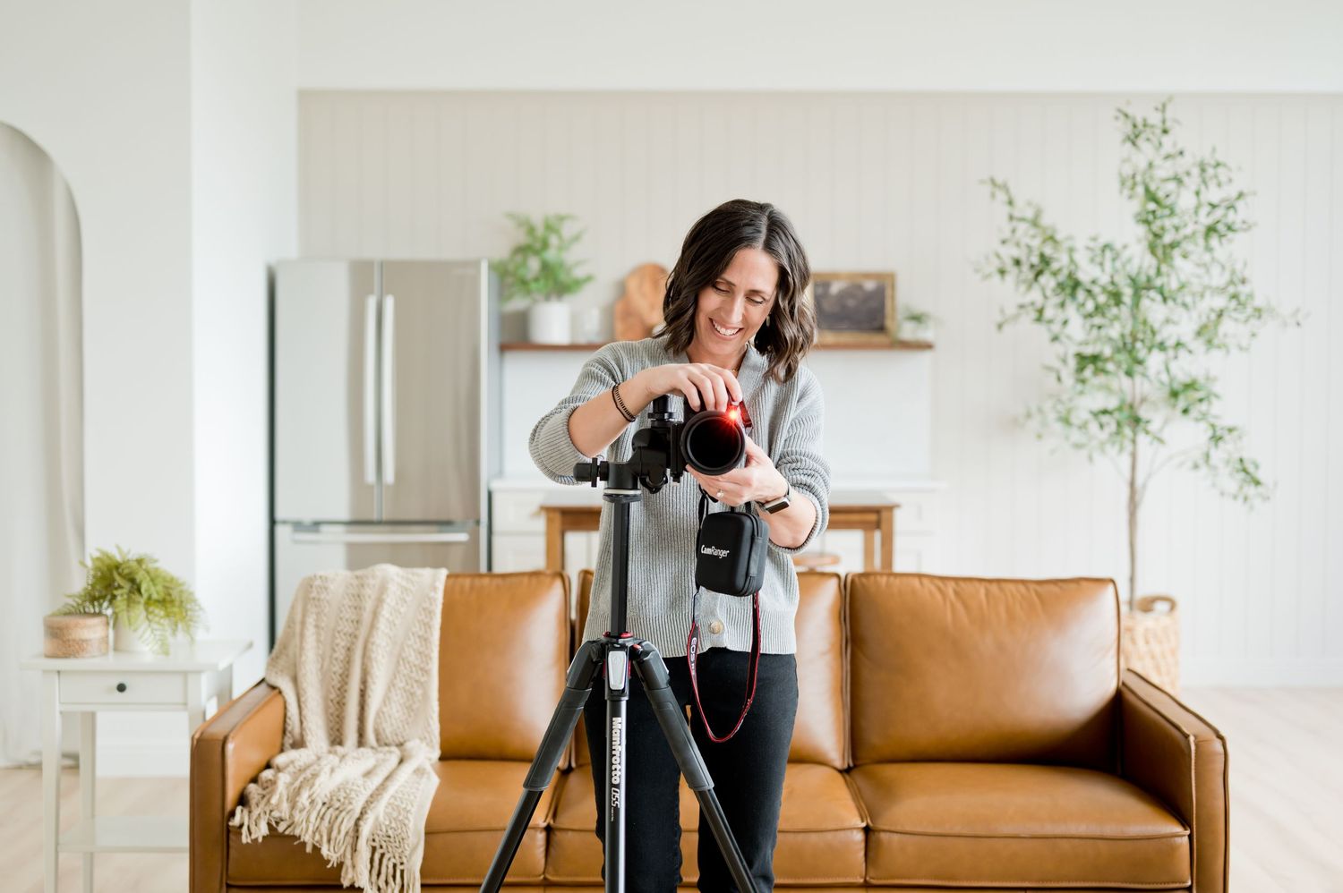 Photographer adjusts camera settings while working with tripod in modern living room setting.