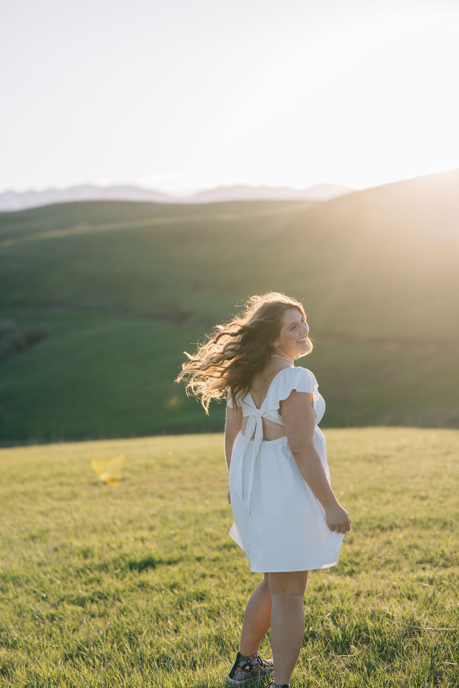 Person in white dress twirling in sunlit meadow during golden hour.