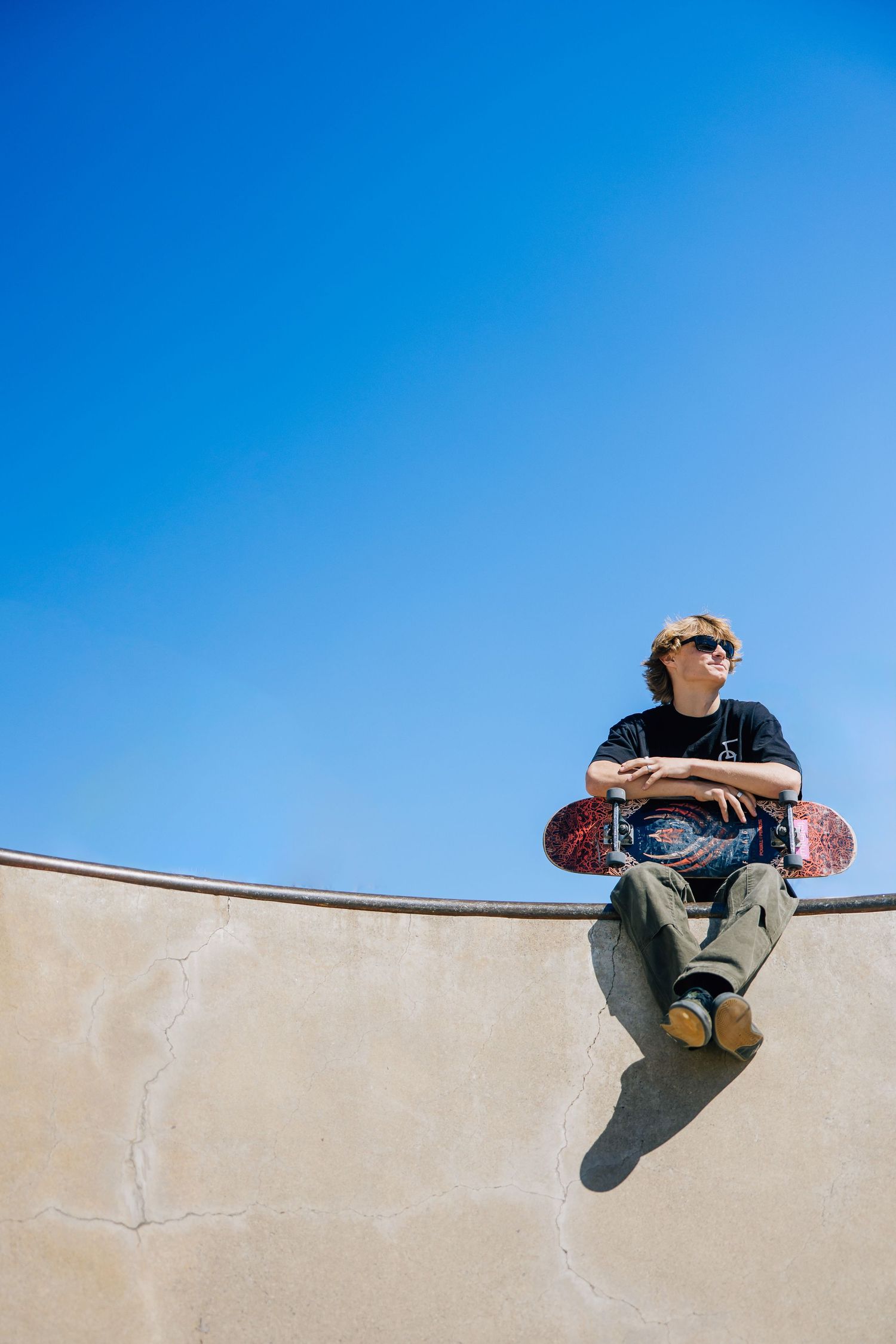 Minimalist composition of legs dangling over concrete wall against bright blue sky.