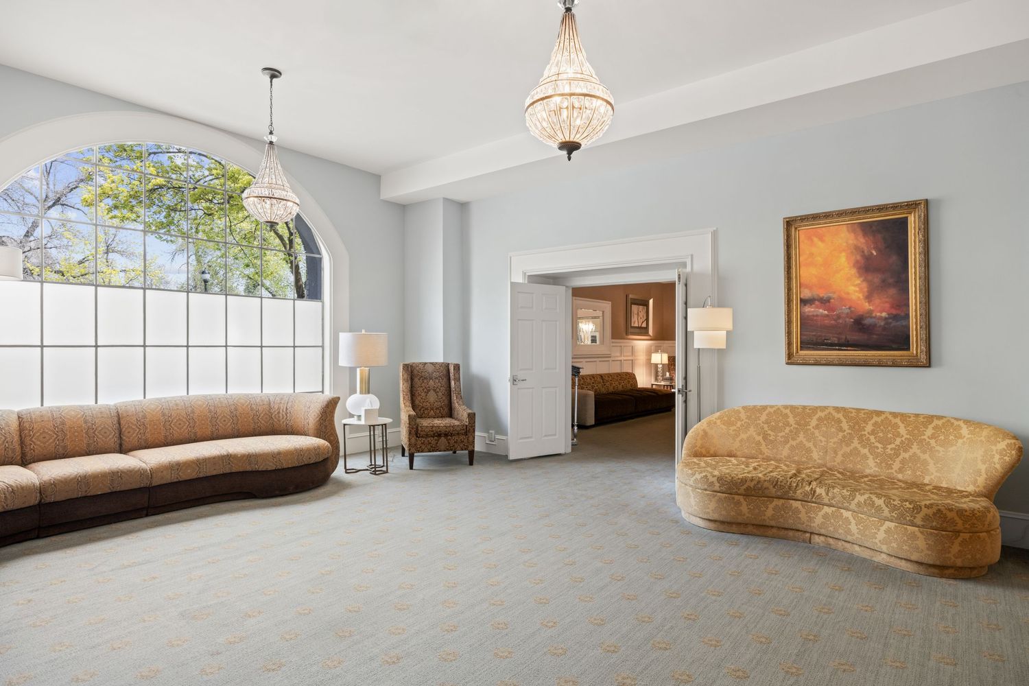 Spacious room with curved sofa, hardwood floors, and elegant chandelier lighting.