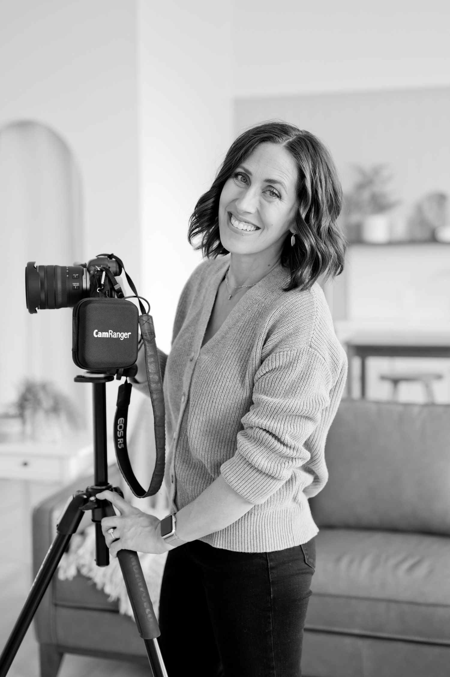 Professional photographer with wavy hair smiles while working with camera equipment in a bright indoor setting.