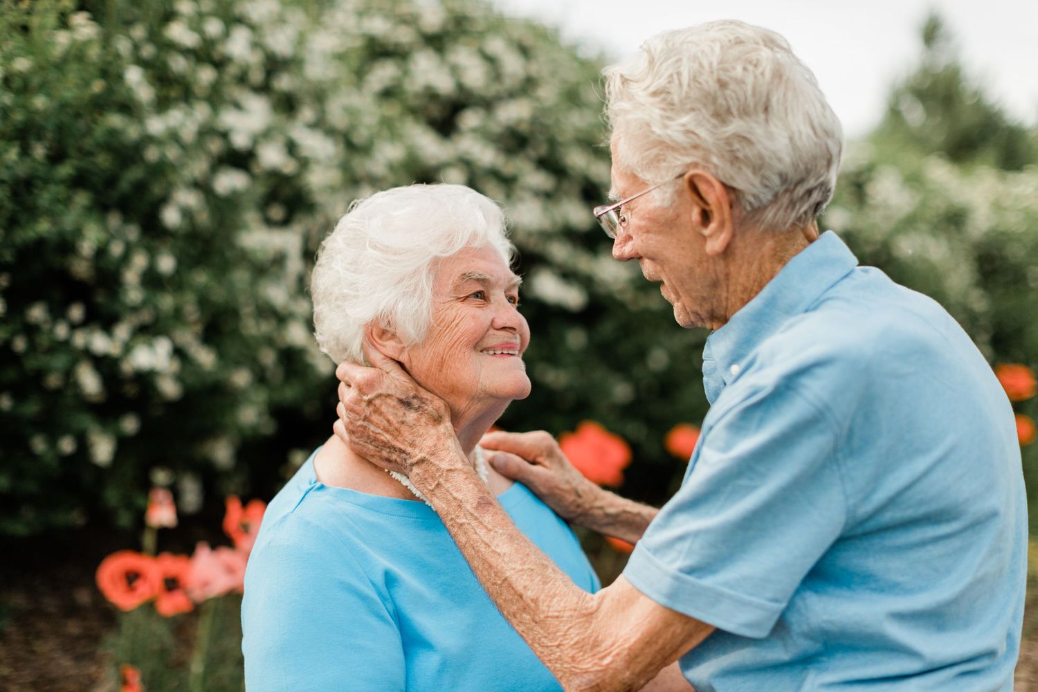 Elderly couple in blue shirts embracing tenderly outdoors with natural background.