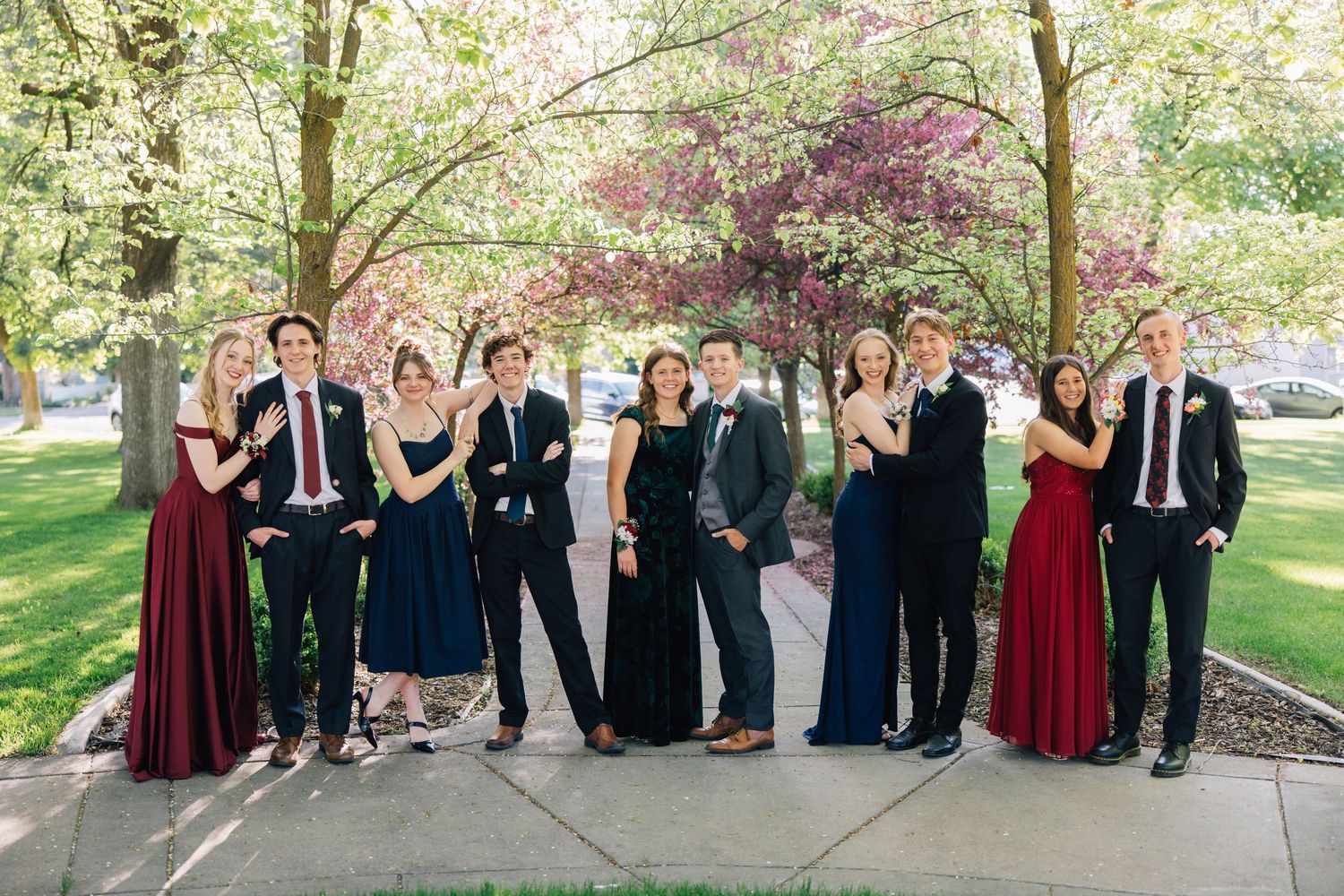 Wedding party group photo with formal attire in front of blooming spring trees.