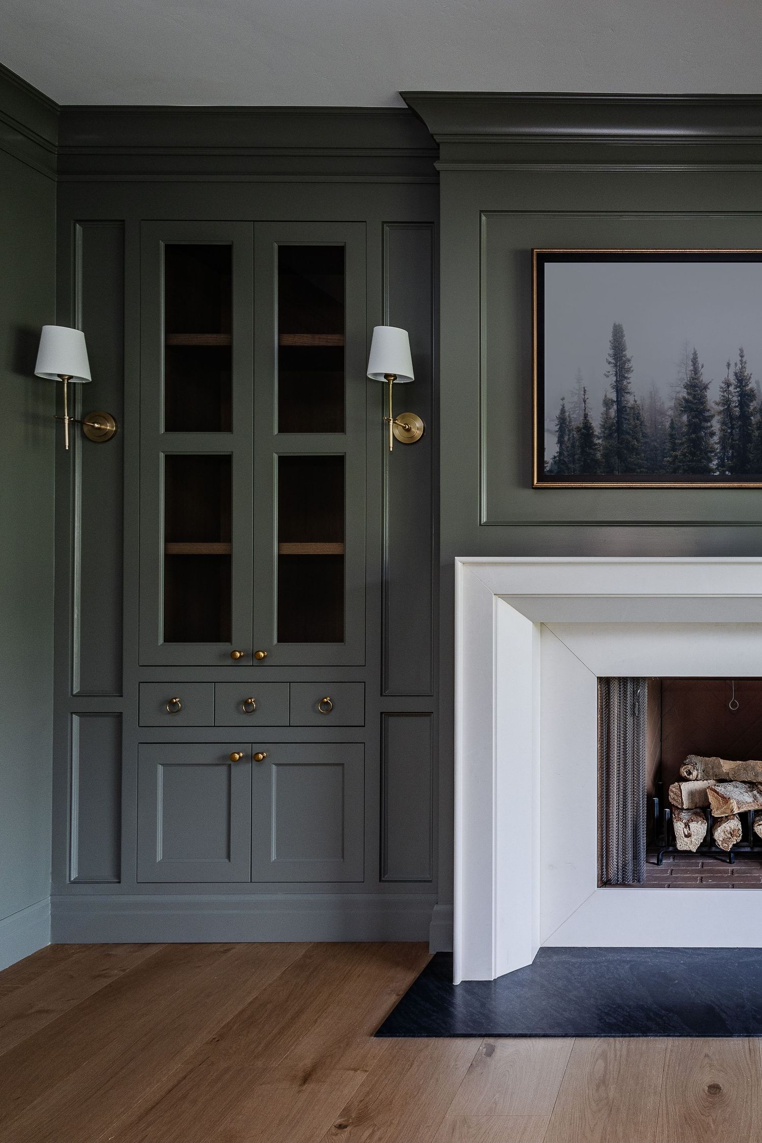 Dark green built-in cabinets with brass hardware line the walls of a contemporary living room with hardwood floors.