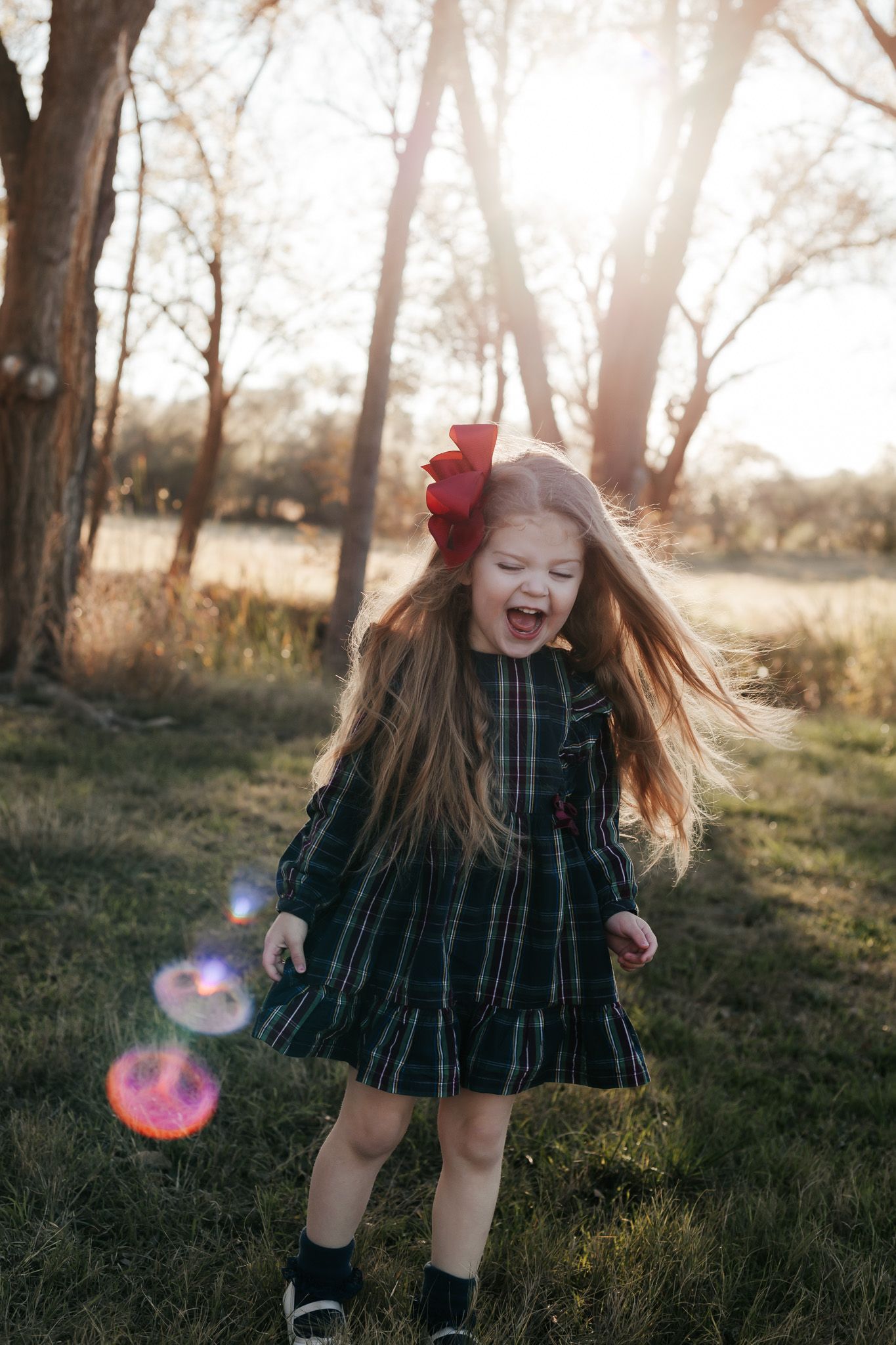 Young child in plaid dress laughing and playing outdoors with bubbles.