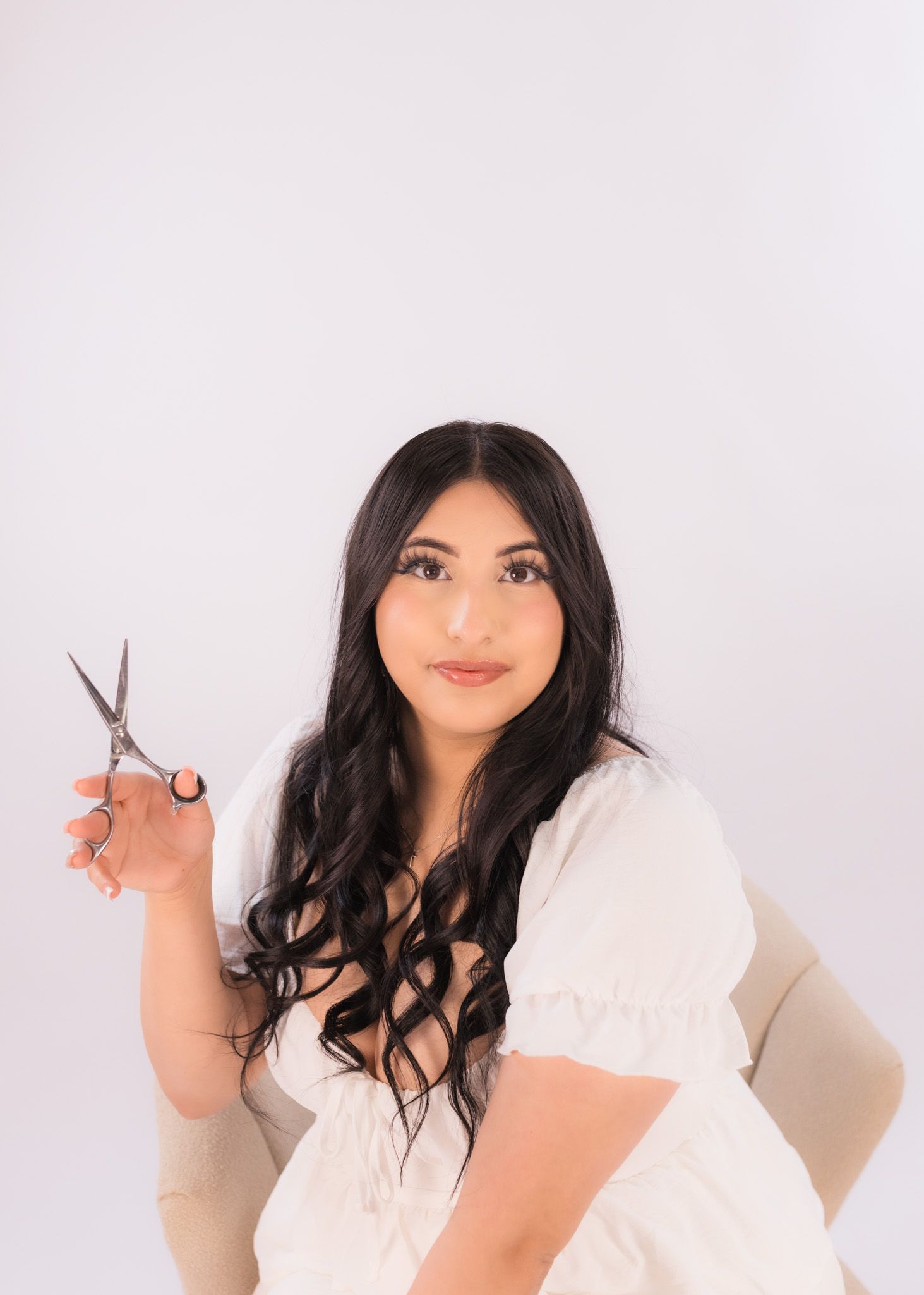 Portrait of woman in white dress holding scissors against light pink background.