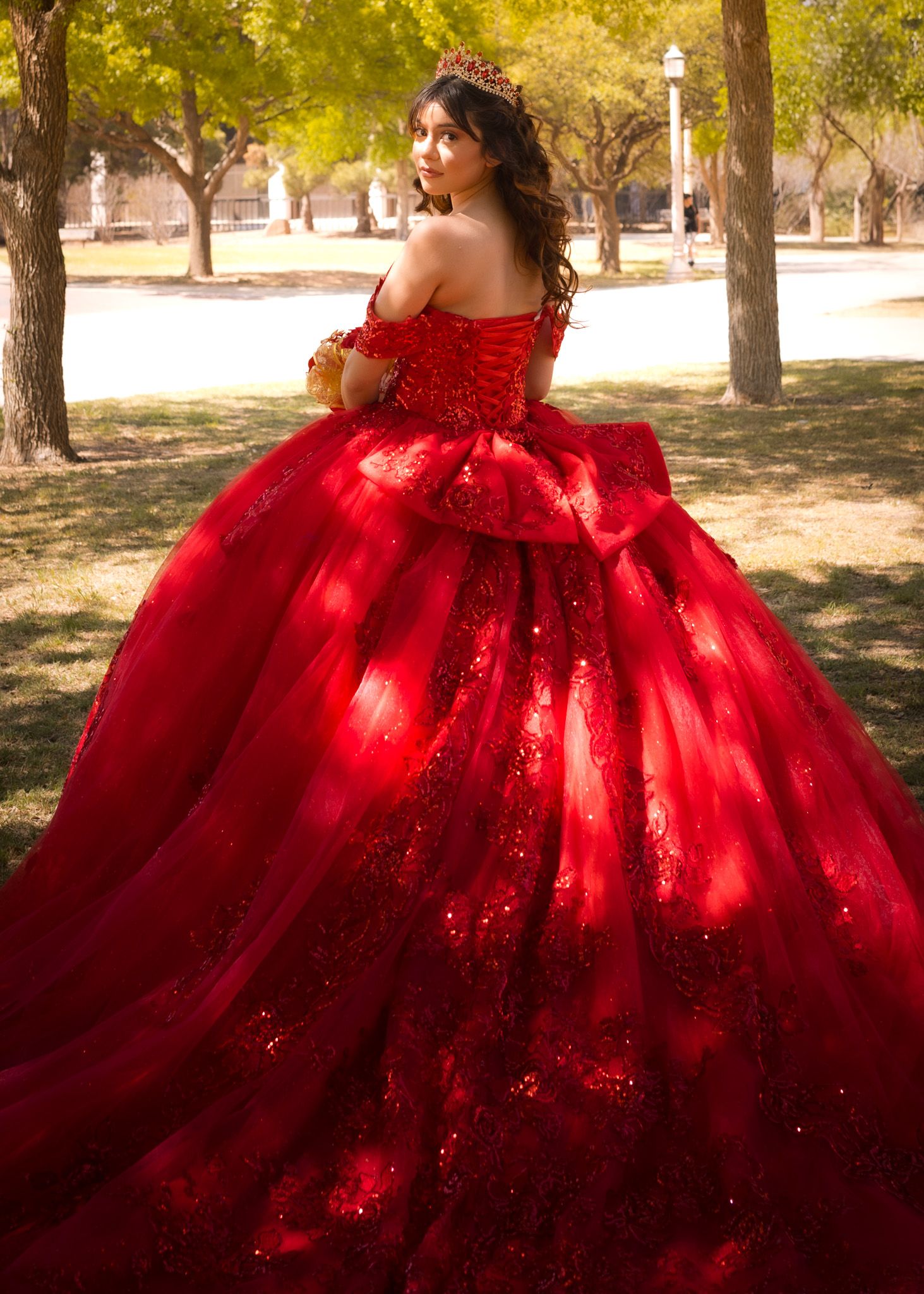 A stunning red ball gown with a voluminous tulle skirt sparkles in the sunlight against a backdrop of autumn trees.
