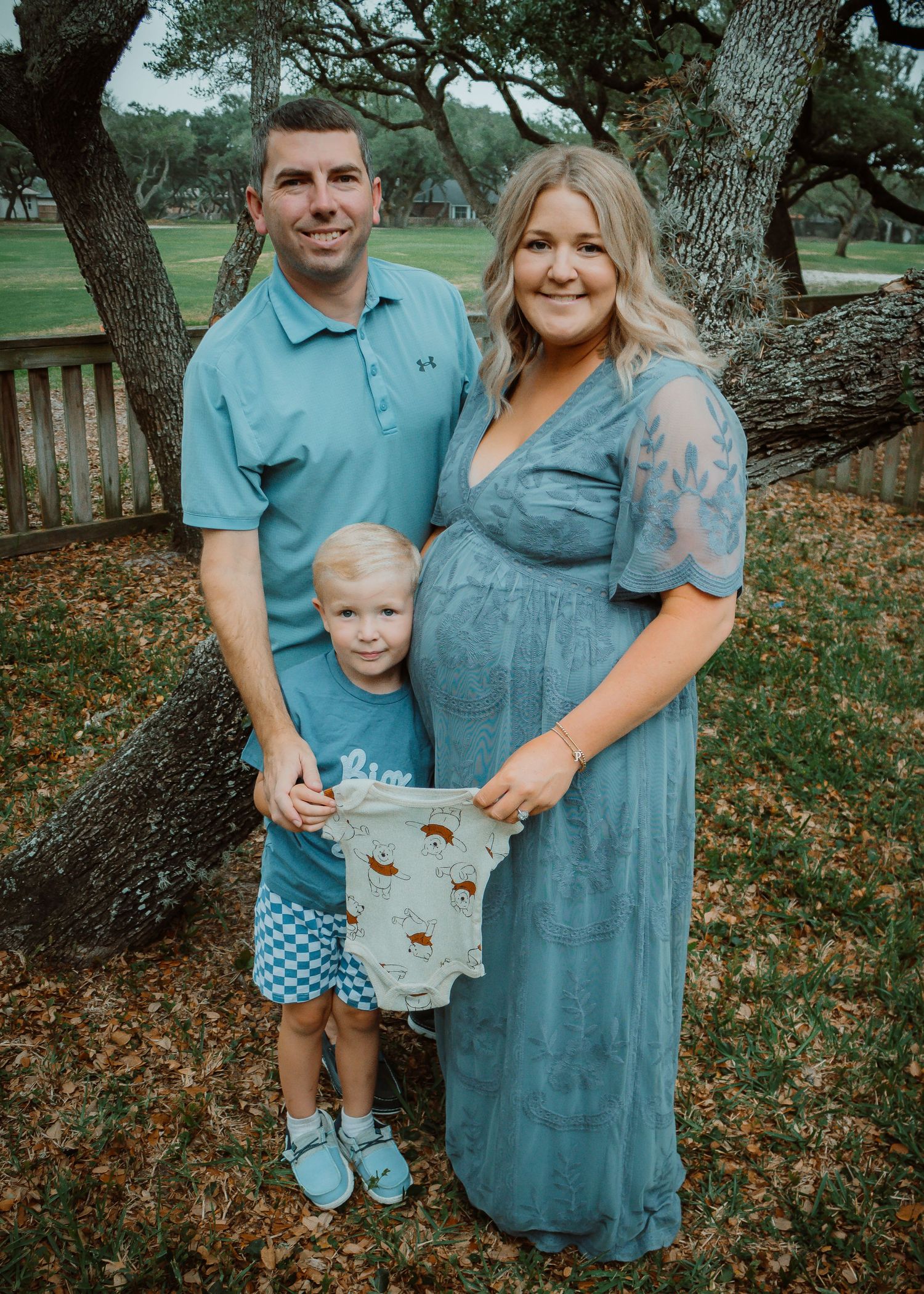 Family pregnancy announcement photo outdoors holding baby clothes.