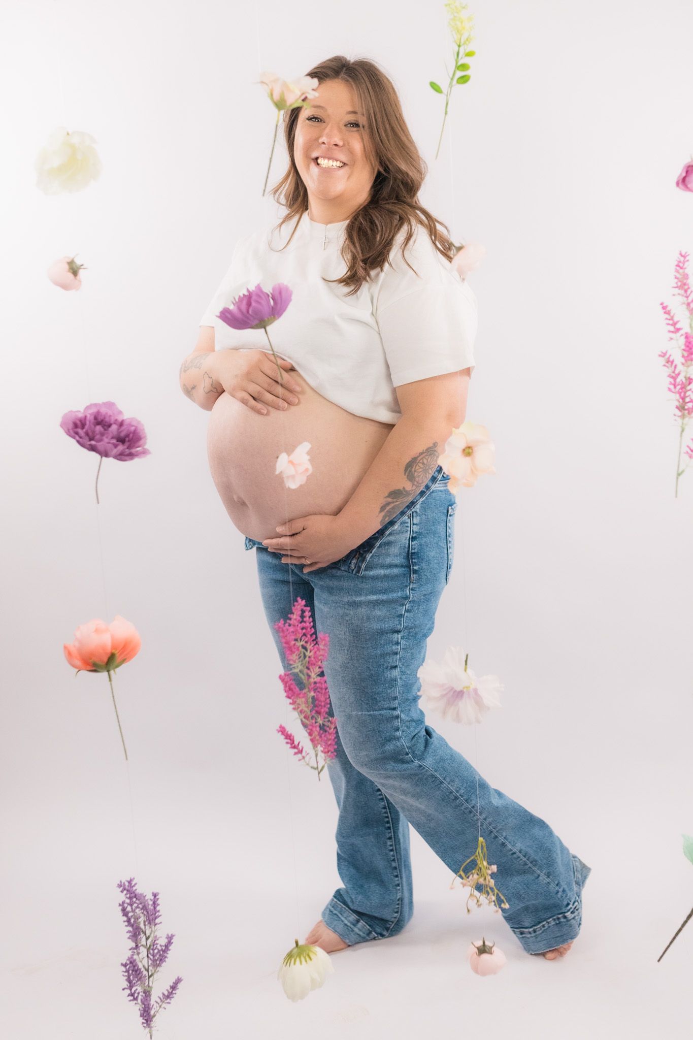Joyful maternity photo surrounded by floating purple and pink flowers.