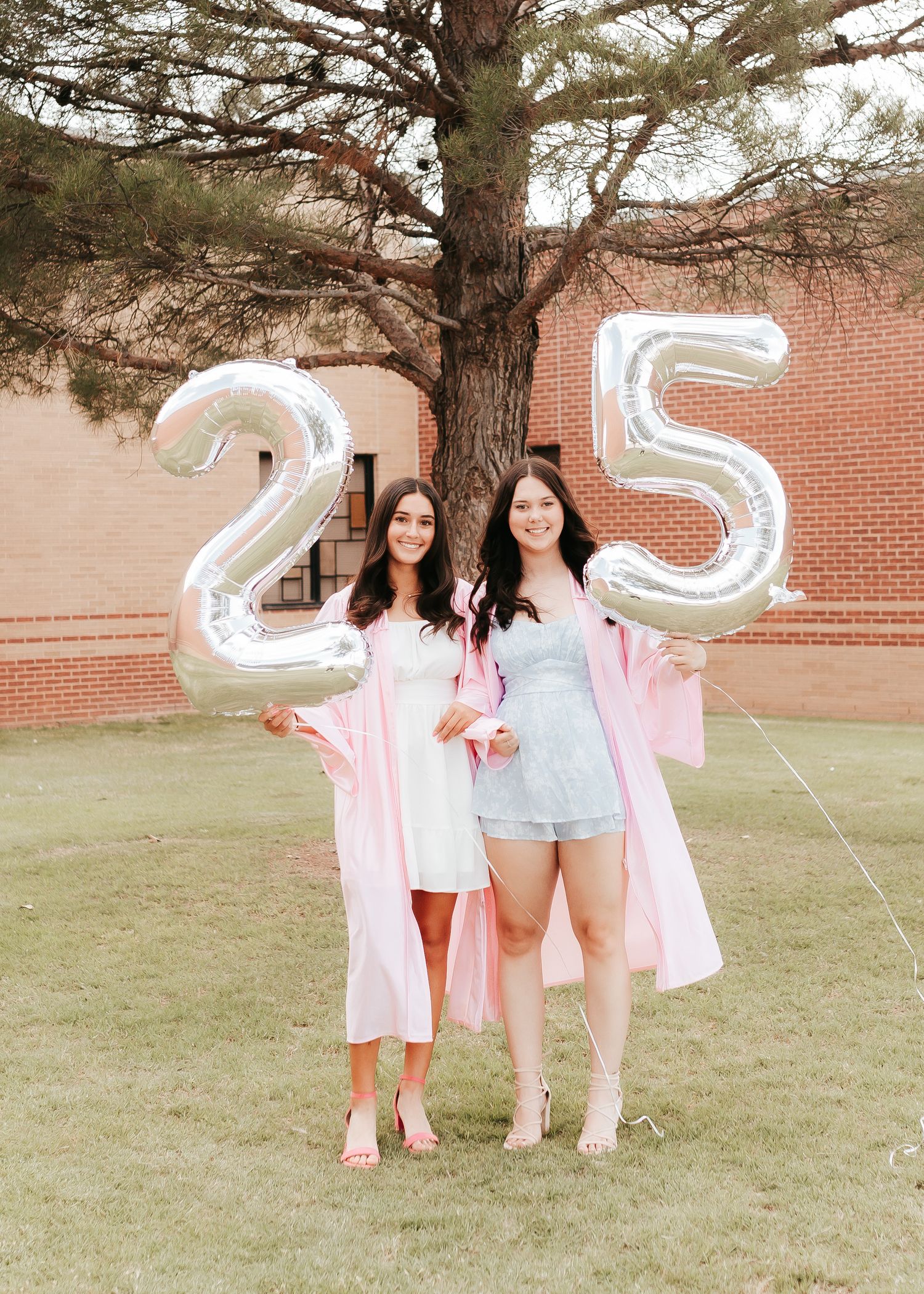 Graduation celebration with large silver number balloons spelling '25' and pink graduation gowns.