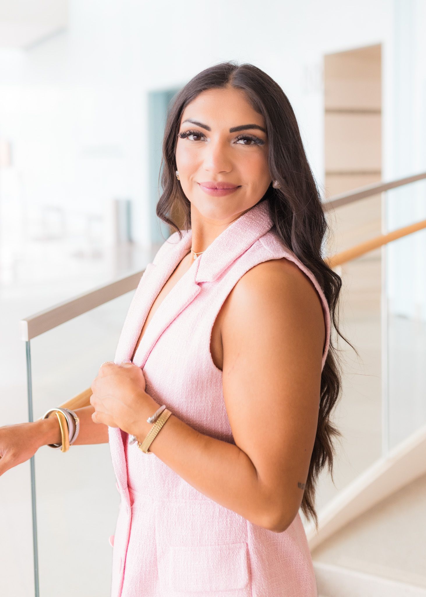 Woman in pink sleeveless top smiles while standing in stairwell.