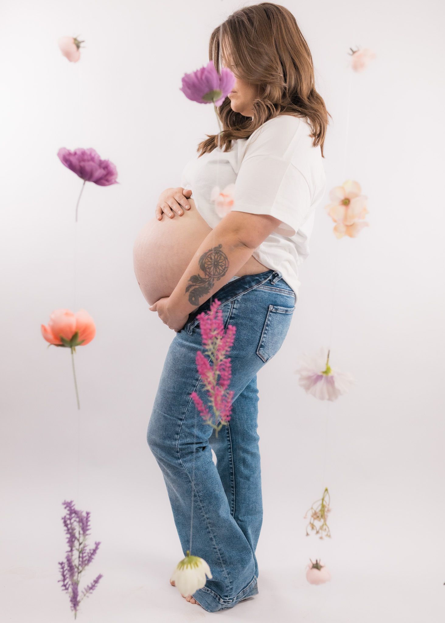 Artistic maternity portrait with floating colorful flowers and exposed pregnant belly.