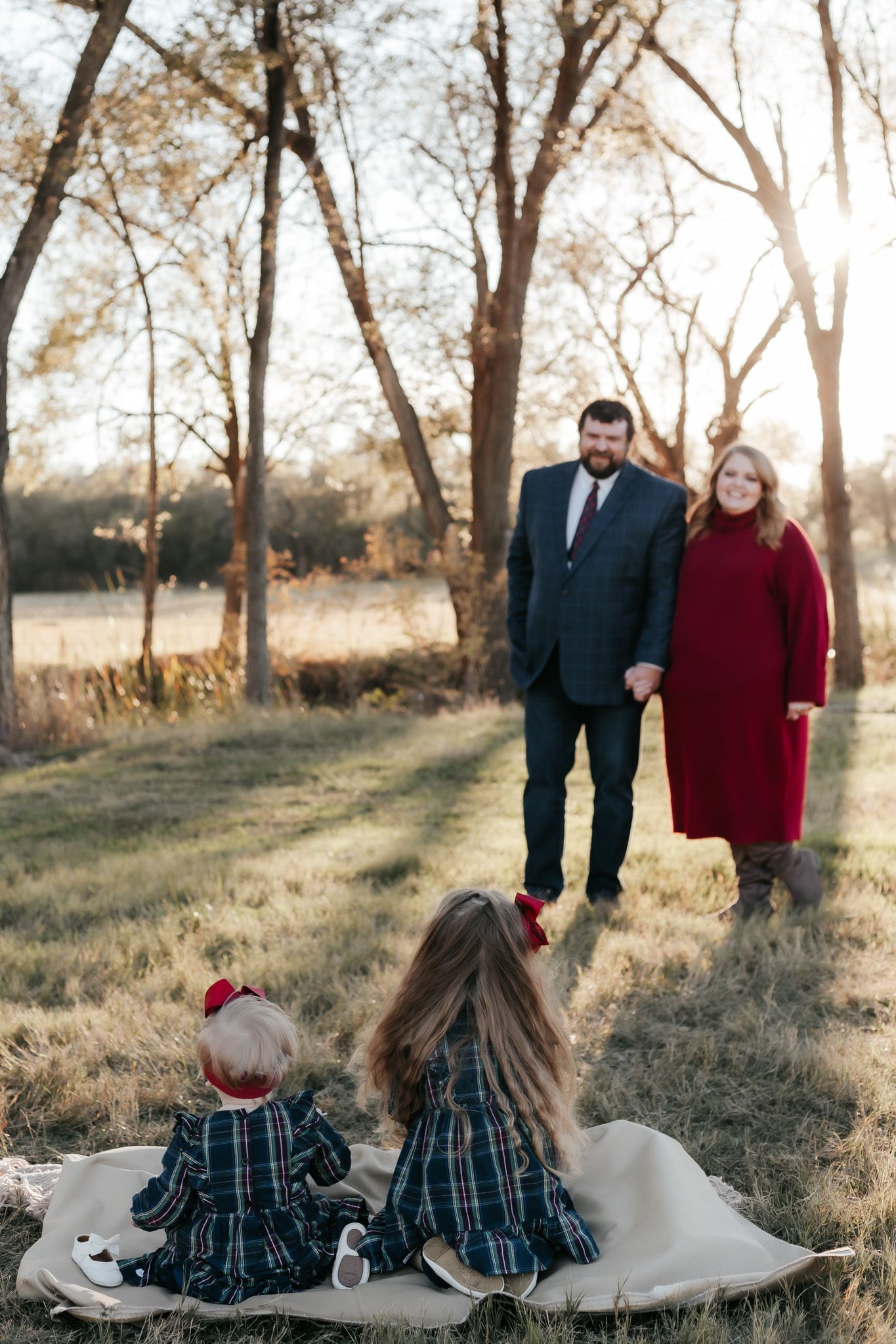 Parents standing while children sit on blanket during outdoor family photoshoot.