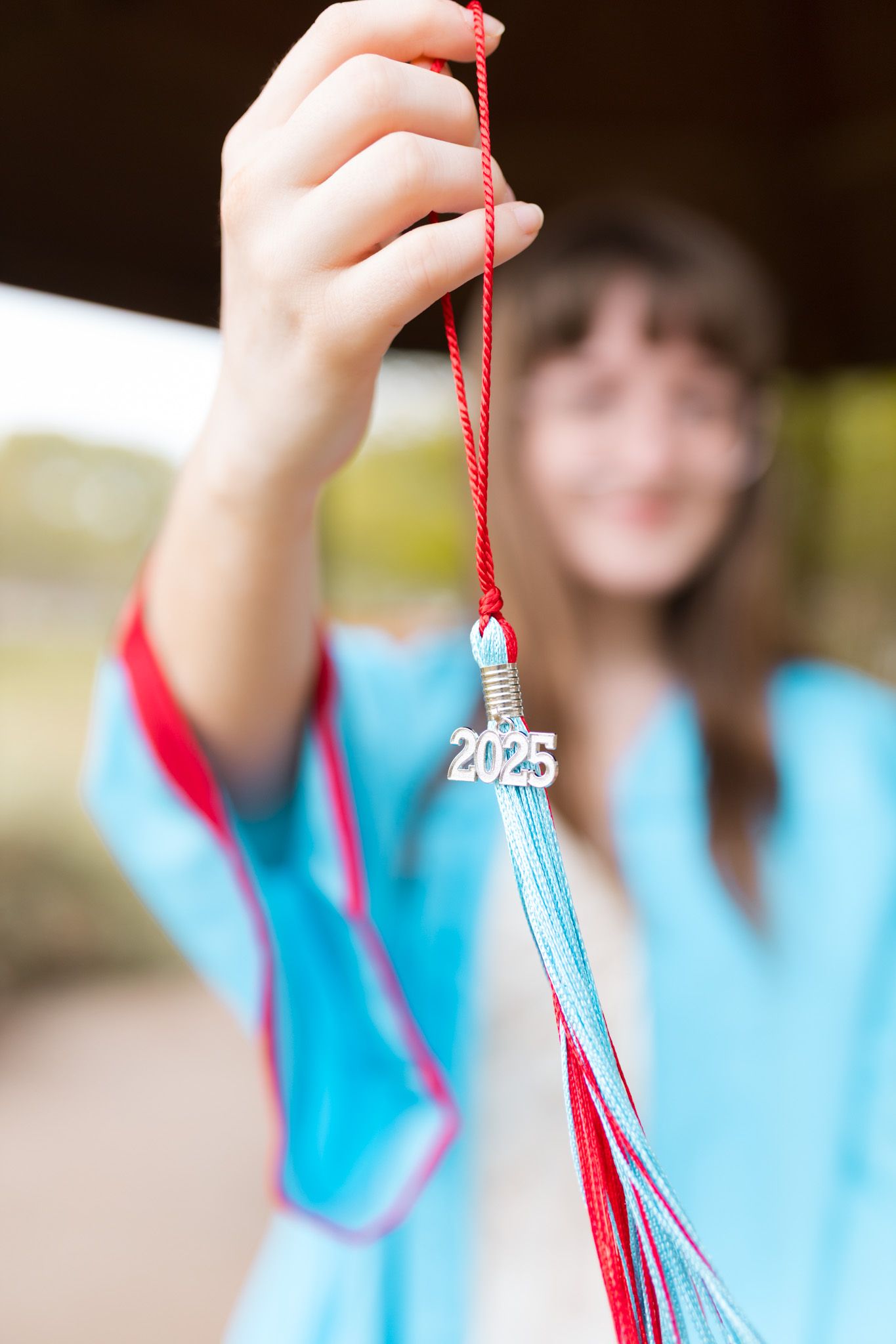 Hand holds graduation tassel with 2023 charm against blurred background.
