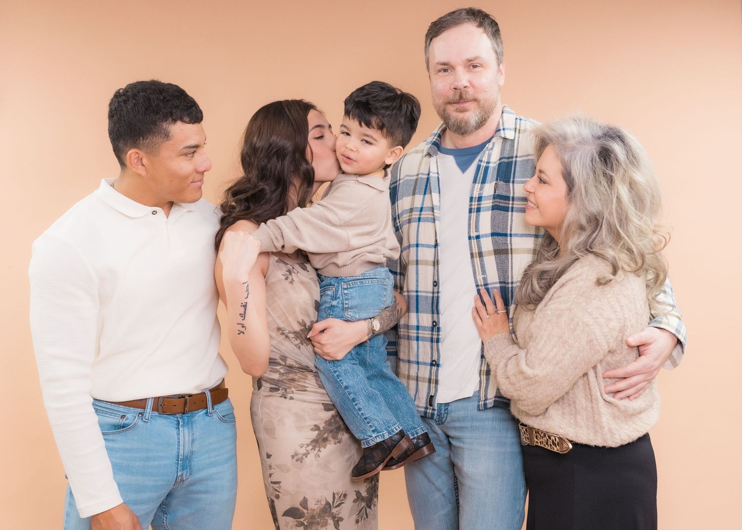Family of five posing together, smiling warmly against a beige background in casual outfits including jeans and sweaters.