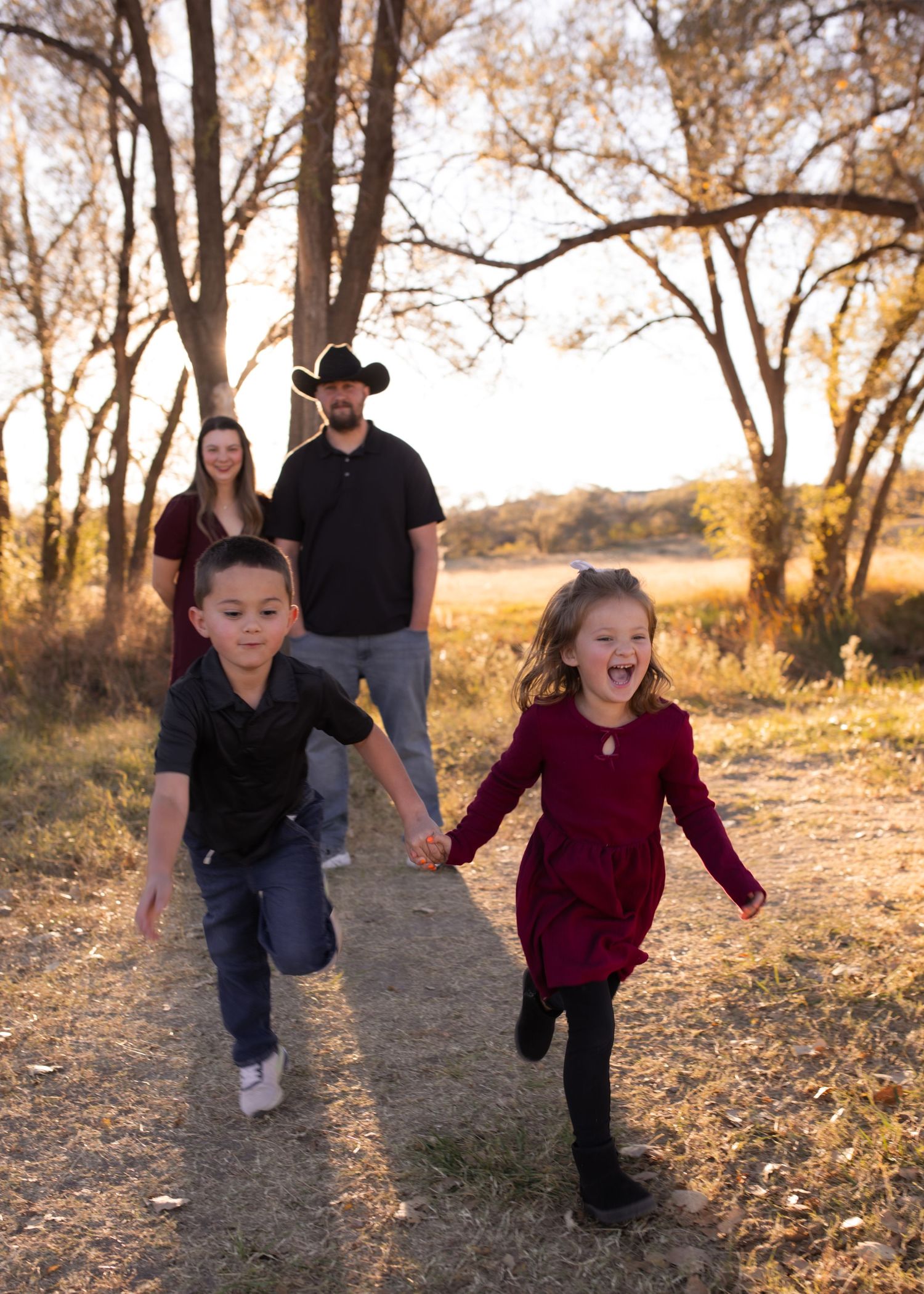 Family of four enjoying a golden hour walk outdoors, two young children running ahead while parents smile behind them.