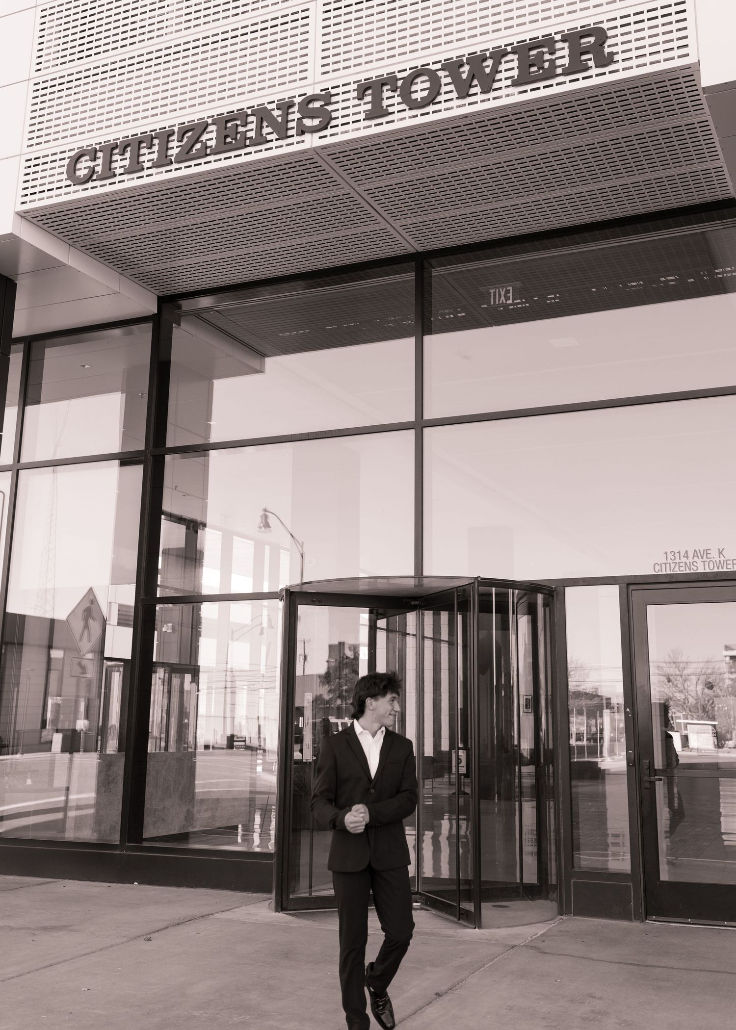 Man in suit exiting Citizens Tower building through revolving doors, black and white professional photo.