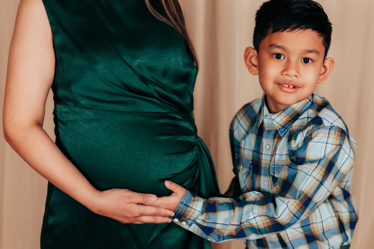 Parent and child share tender moments in a maternity photoshoot wearing dark green and plaid.