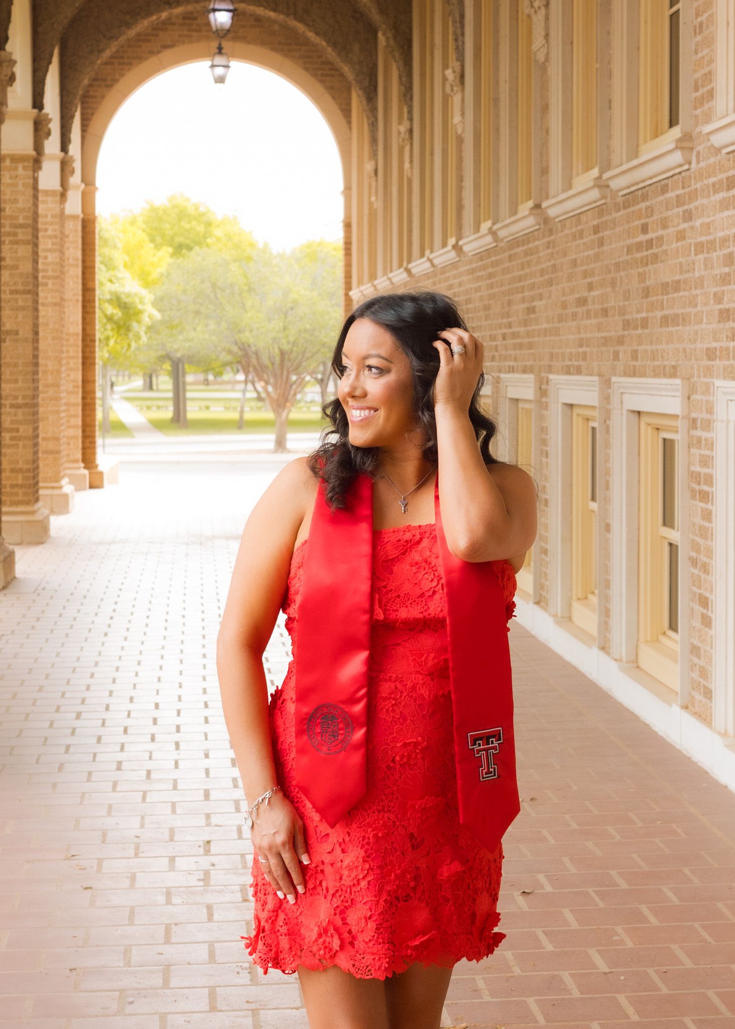 A person in a red lace dress stands in a covered walkway with brick columns.