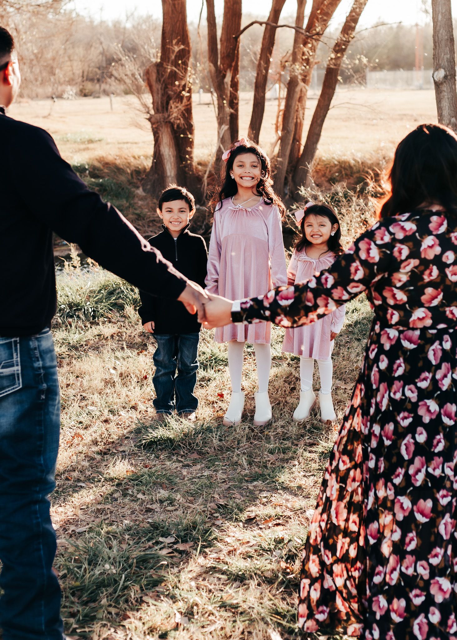 Family photo session outdoors with children in coordinated pink outfits and parents holding hands.