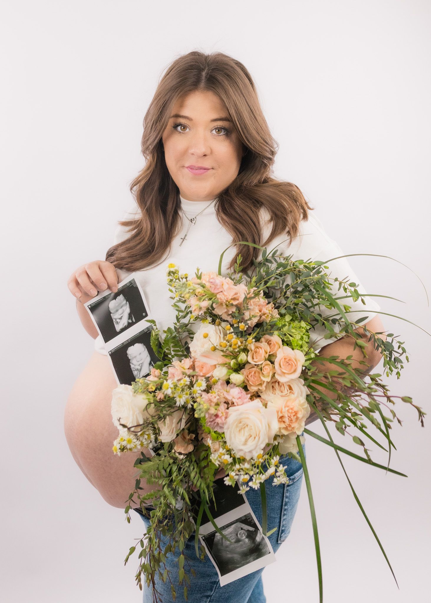 A person holding ultrasound photos and a beautiful peach and white floral bouquet against white background.