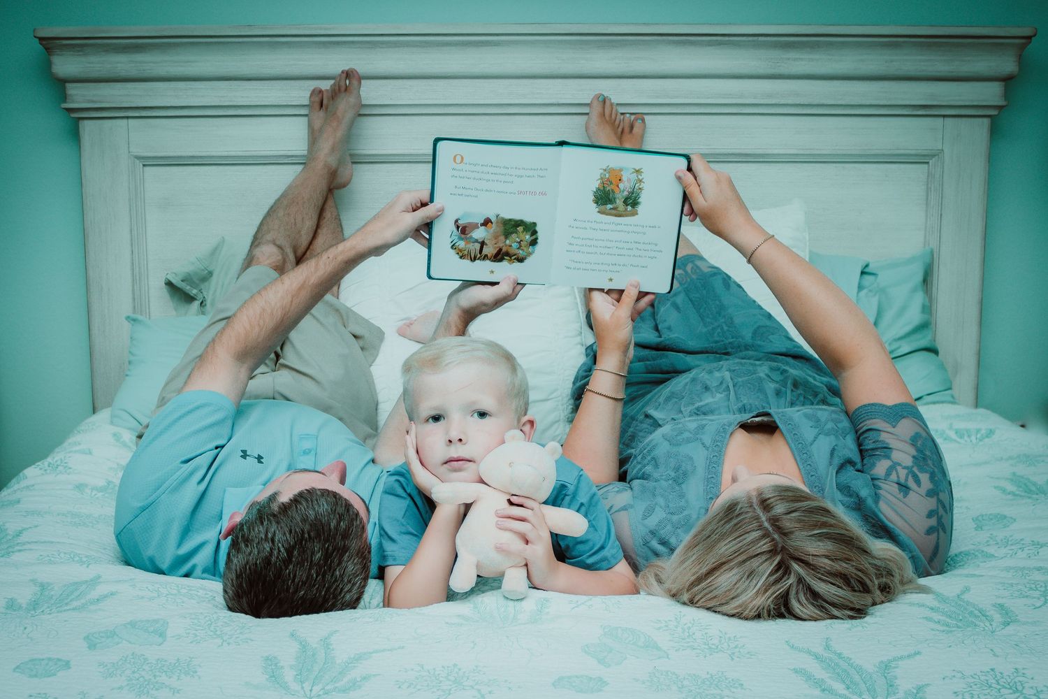 Family reading together on turquoise bed with decorative headboard.