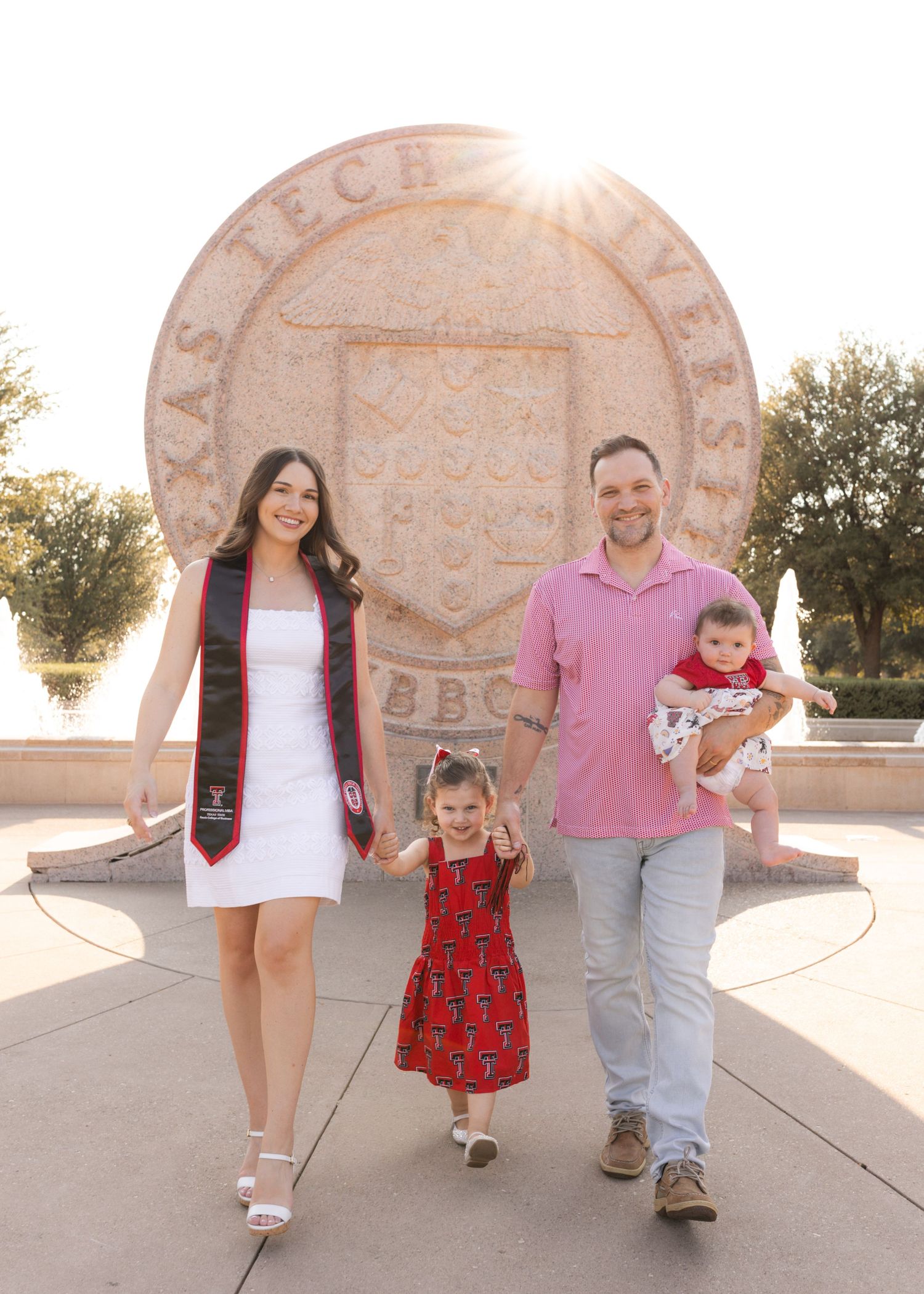 A family celebrates a Texas Tech University graduation, posing in front of the campus seal with two young children.