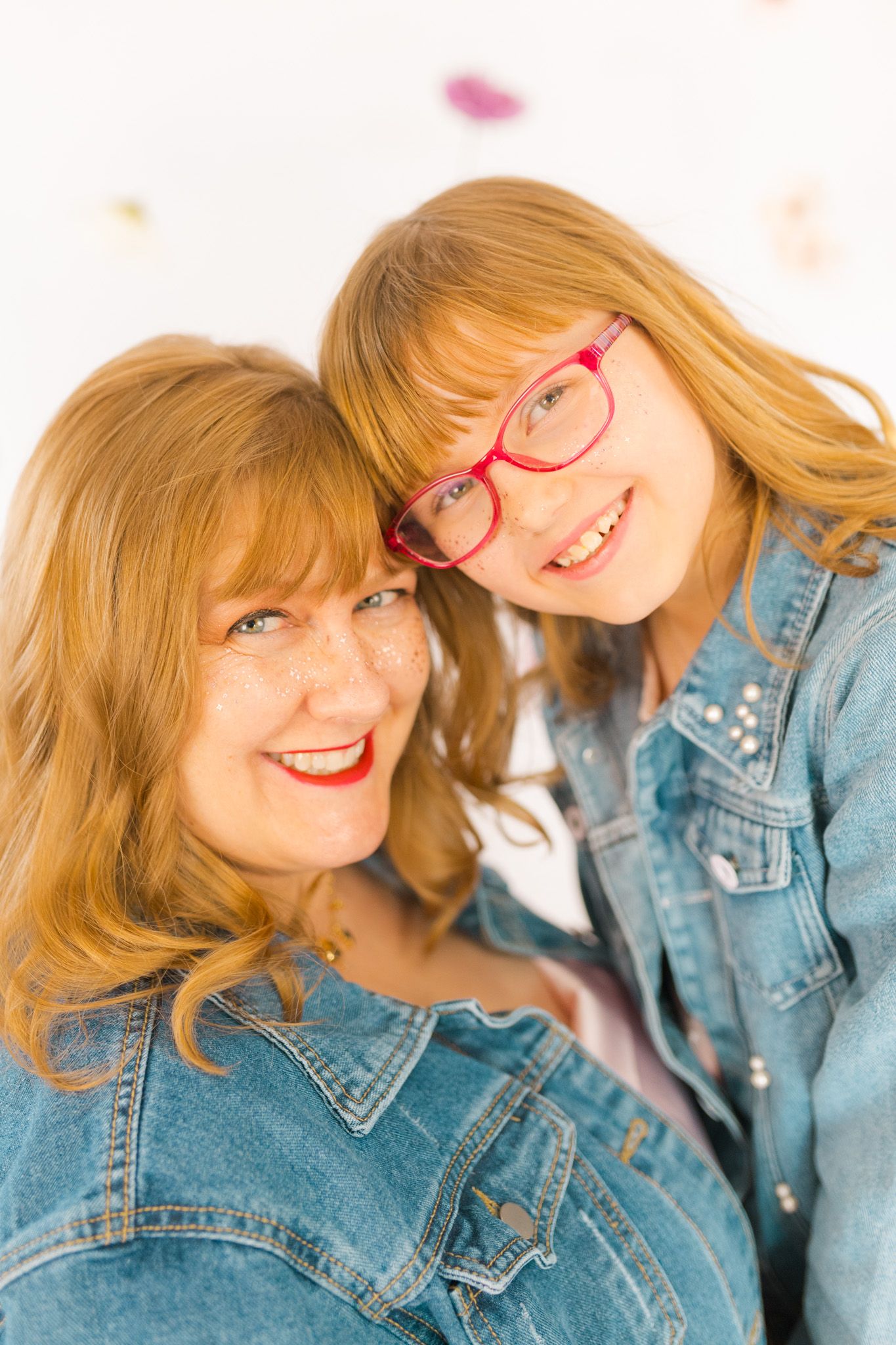 Two people in matching denim jackets share a close affectionate moment against a light background.