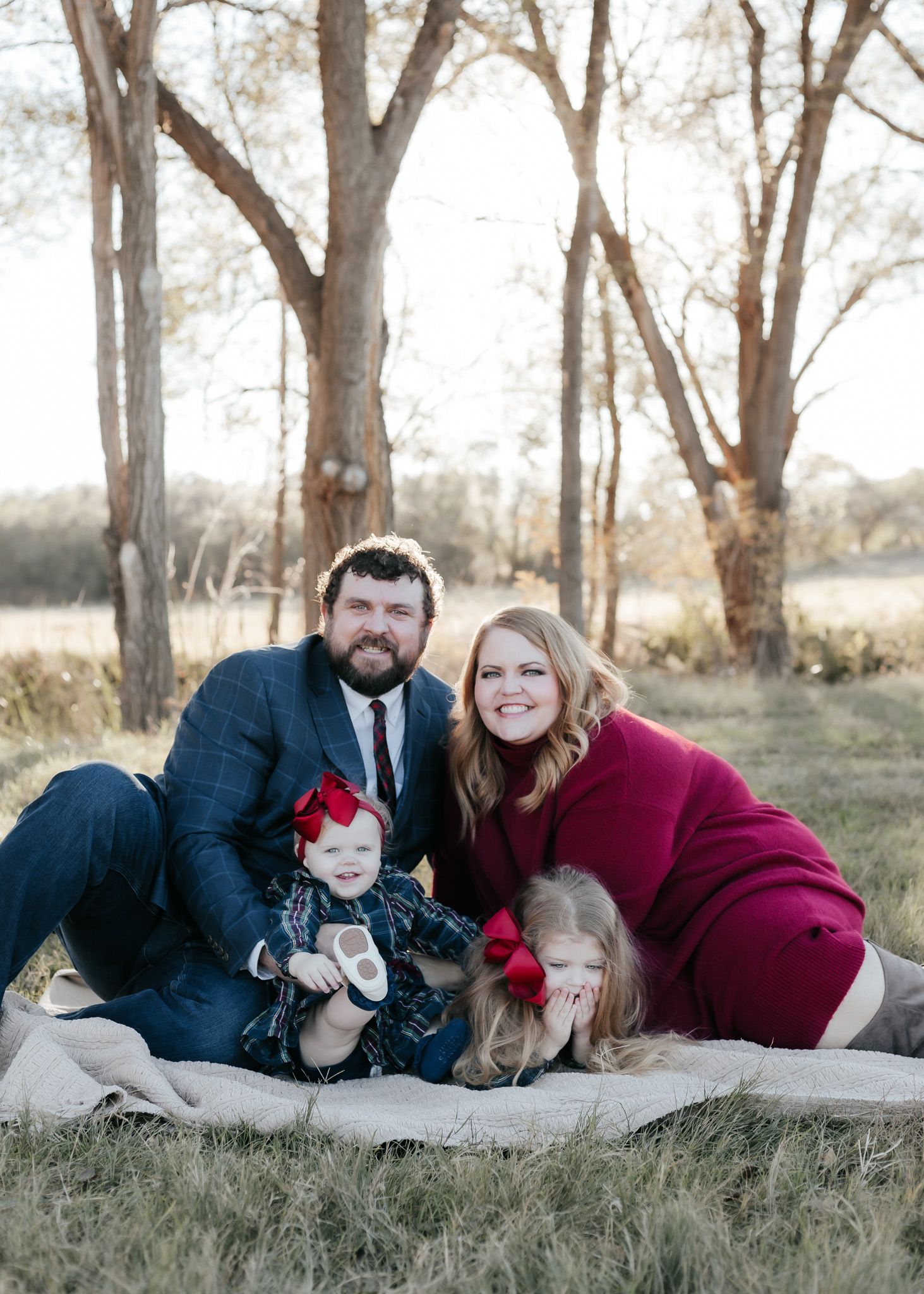 Family of four lying on blanket for outdoor portrait session in wooded setting.
