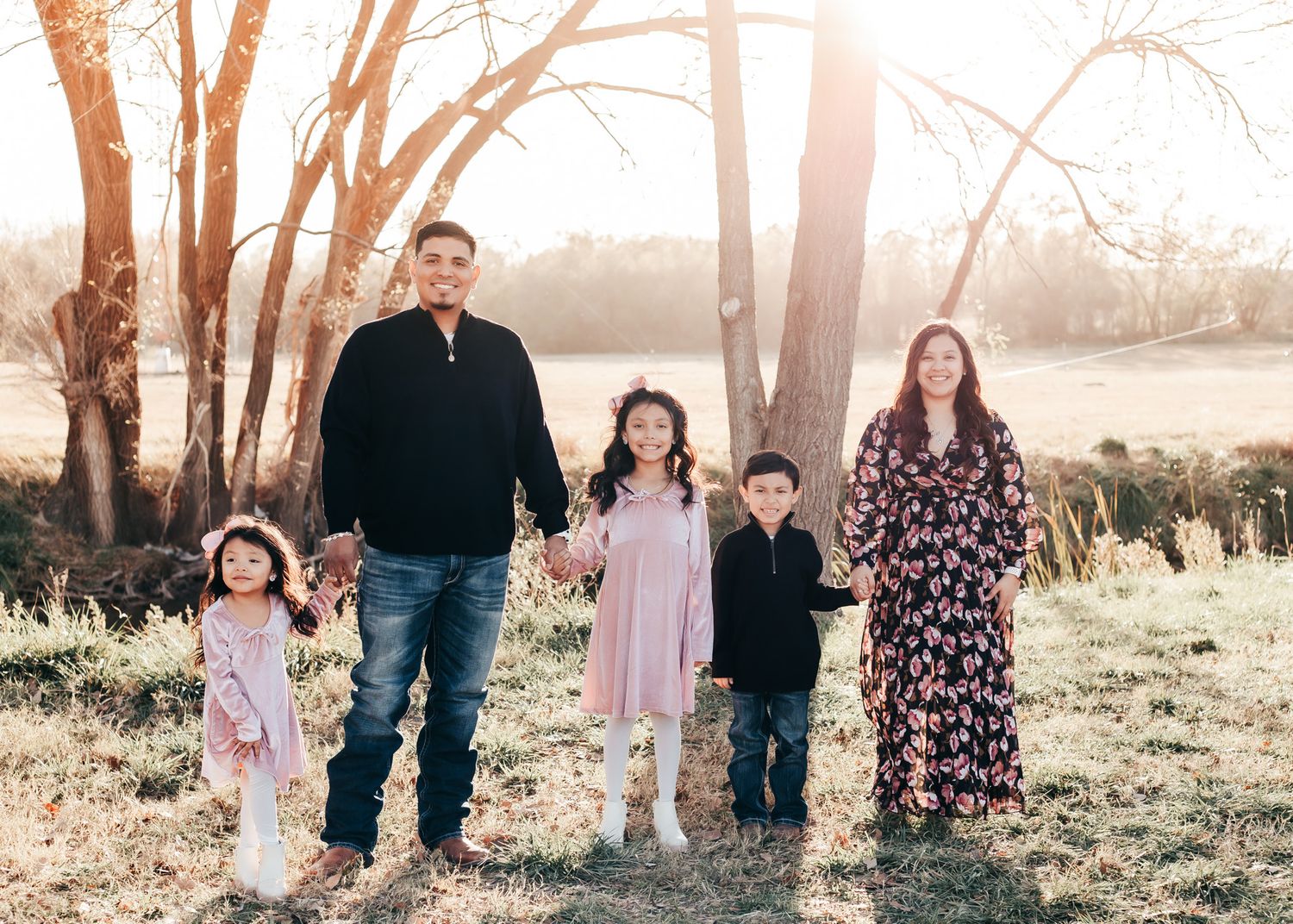 Family of five posing for a portrait in a natural outdoor setting with golden sunlight filtering through trees.