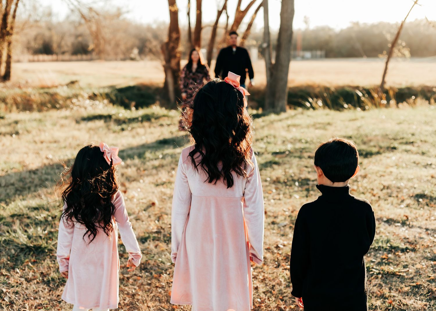 Back view of three children standing together in matching outfits during a sunset photo session.