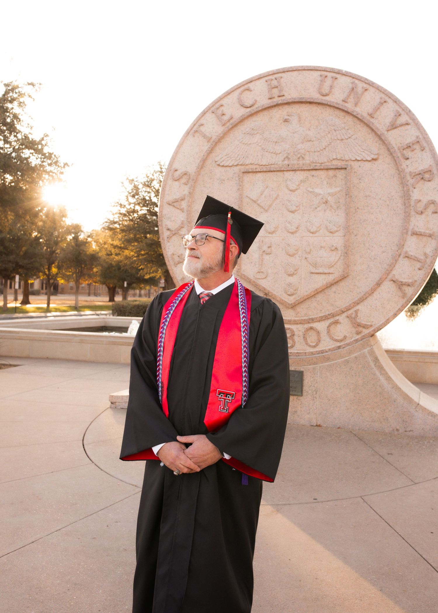 Texas Tech University graduate in black cap and gown stands proudly before the iconic TTU seal in Lubbock.
