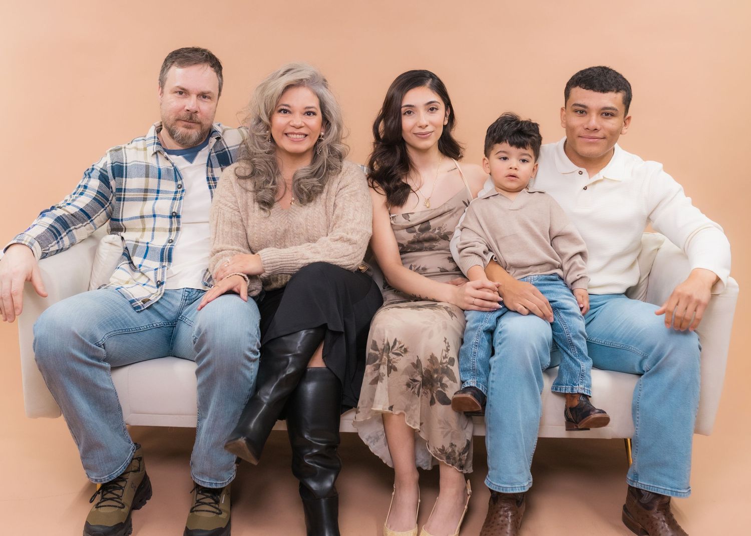 Multi-generational family of five poses together on a white sofa against a warm beige studio backdrop.