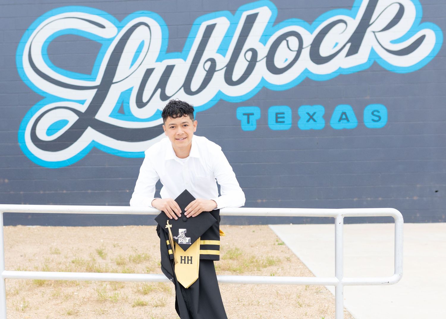 A young person in a white shirt poses in front of a large Lubbock Texas mural sign outdoors.