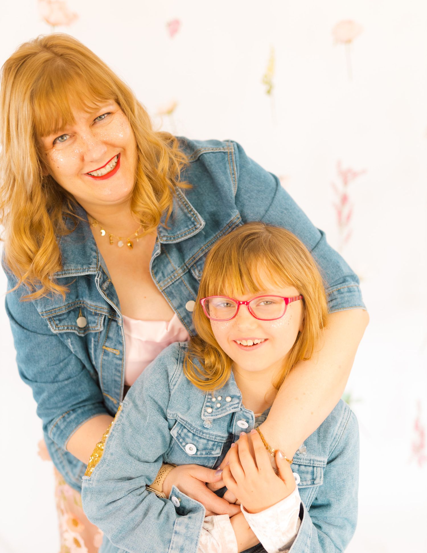 Two people in matching denim jackets pose playfully for a portrait against a white background.