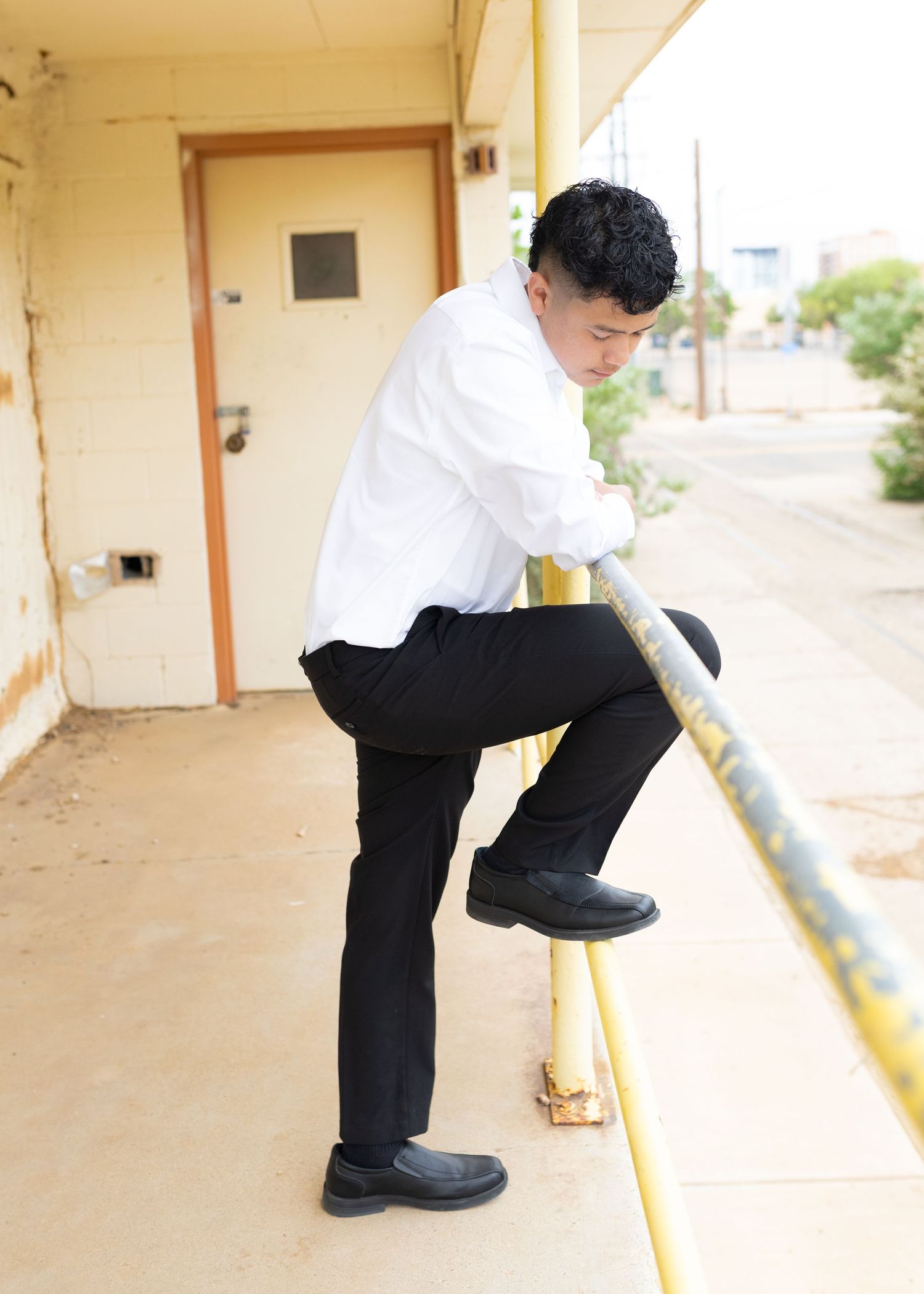 Young man in white shirt and black pants climbing a yellow railing outside a building.