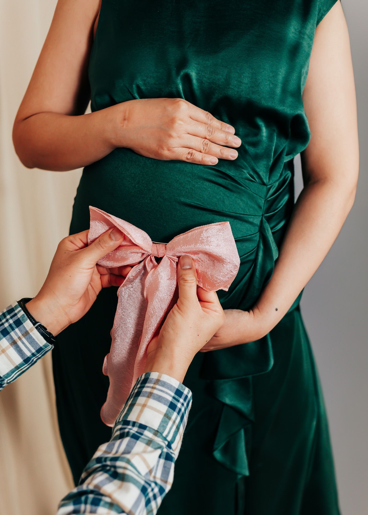 Hands tying pink bow on emerald green maternity dress in intimate moment.