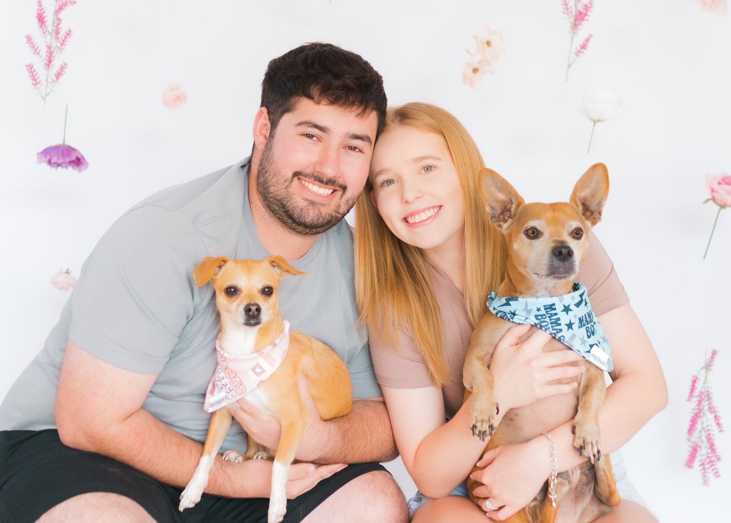 Couple poses with their two small dogs against floral backdrop in studio.