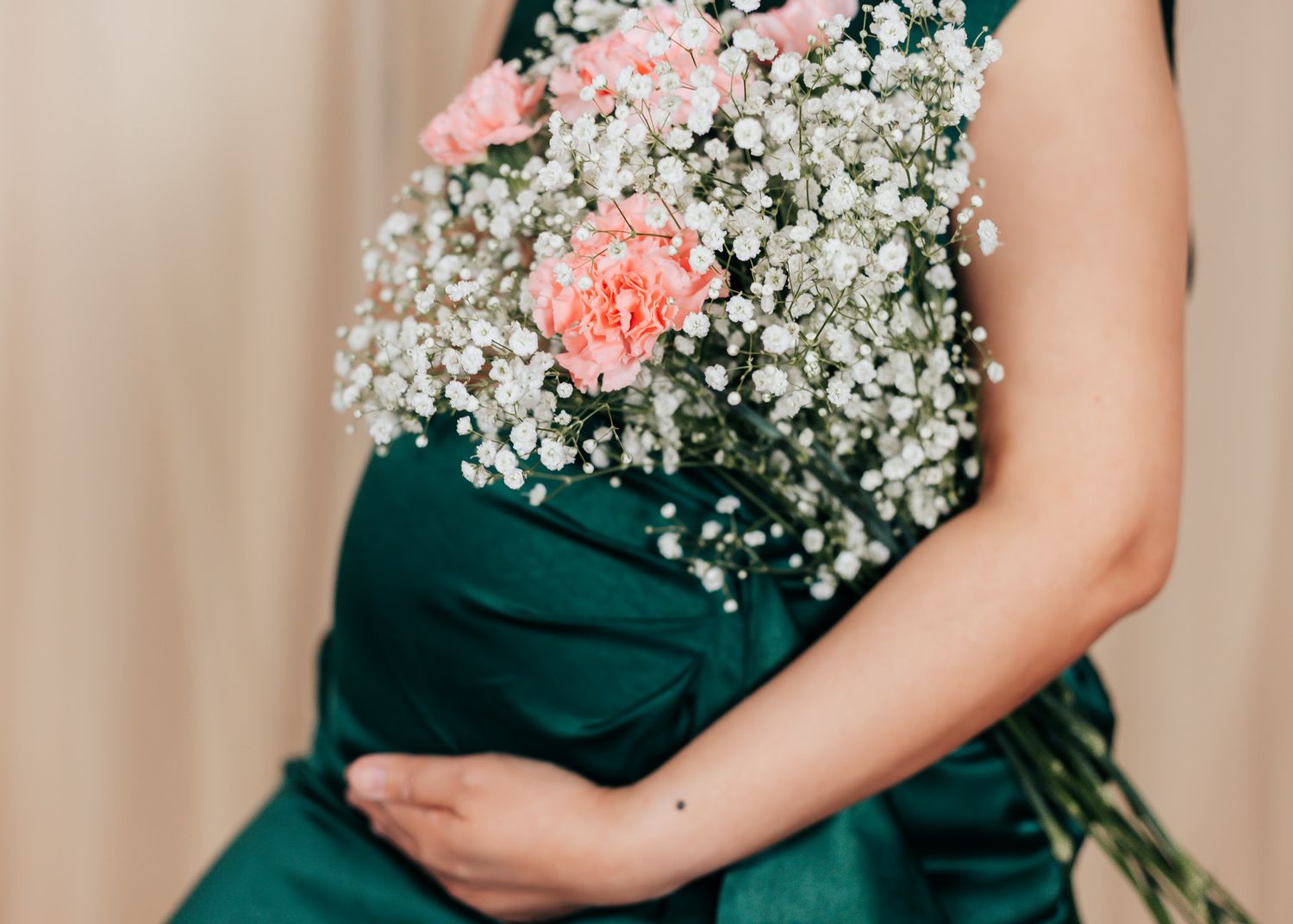Maternity photos with delicate baby's breath and pink carnation flowers against a dark green dress.