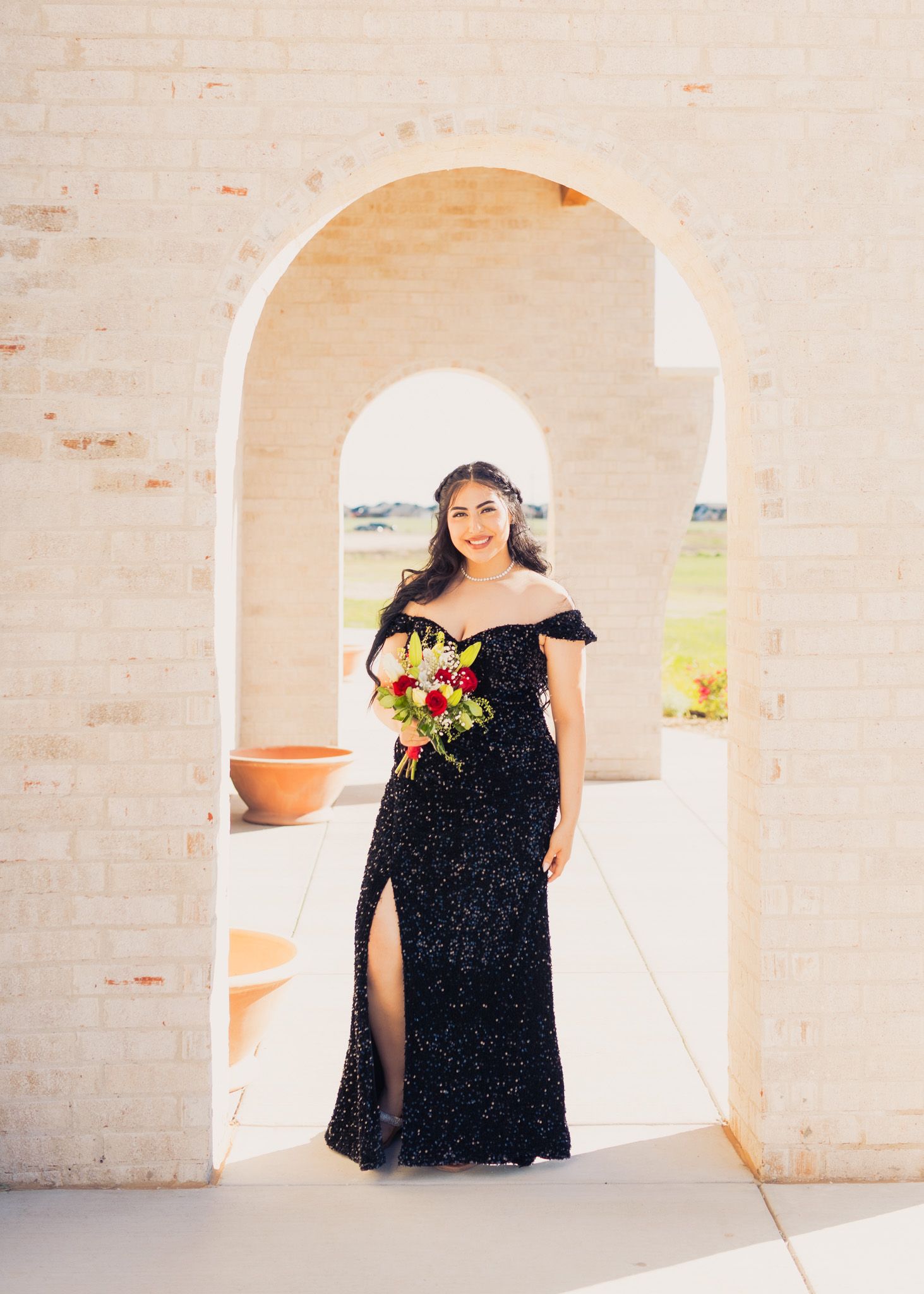 Formal portrait under cream archway wearing black sequined gown with floral bouquet.