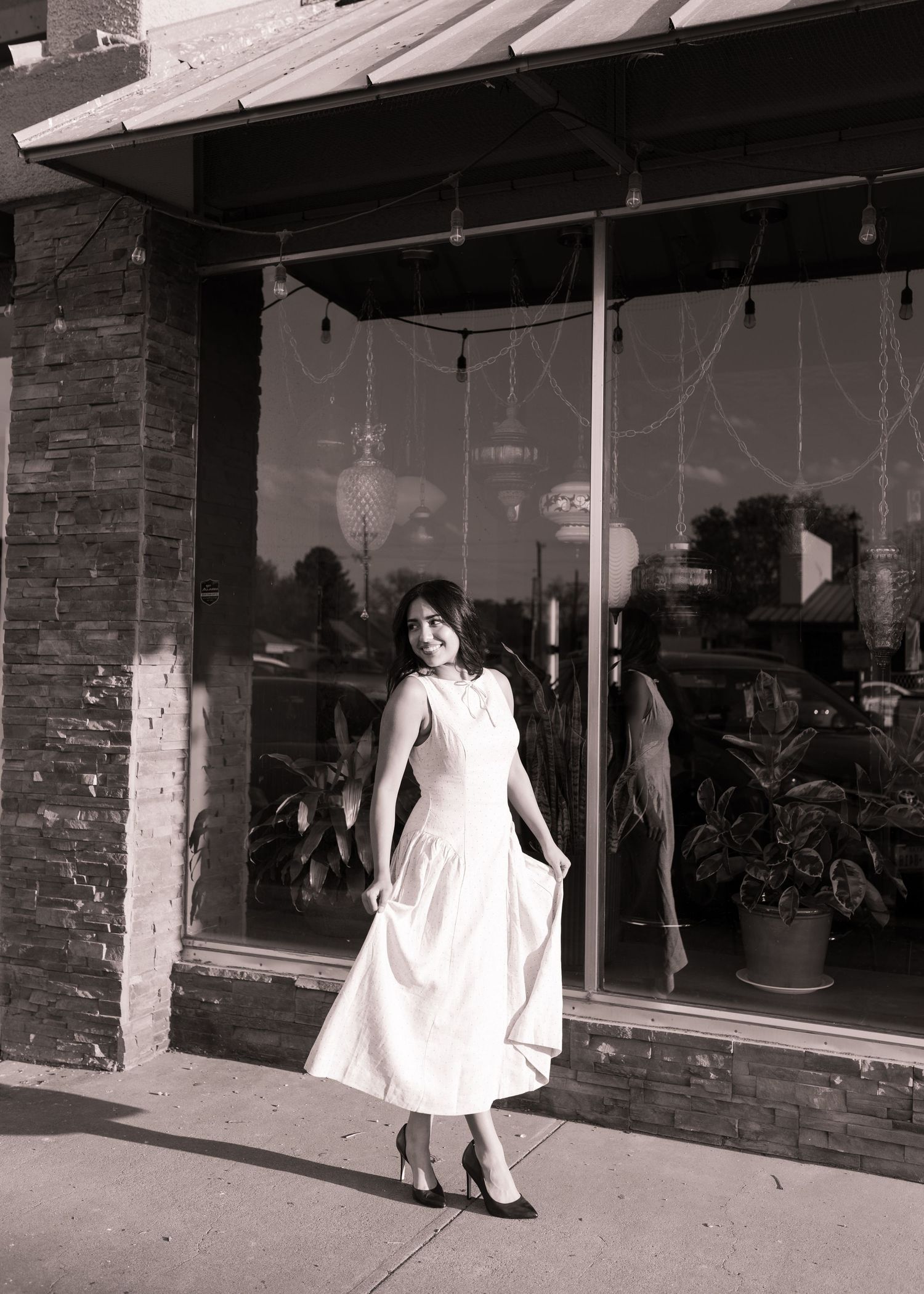 Woman in white midi dress posing and twirling outside a storefront in a black and white photo.